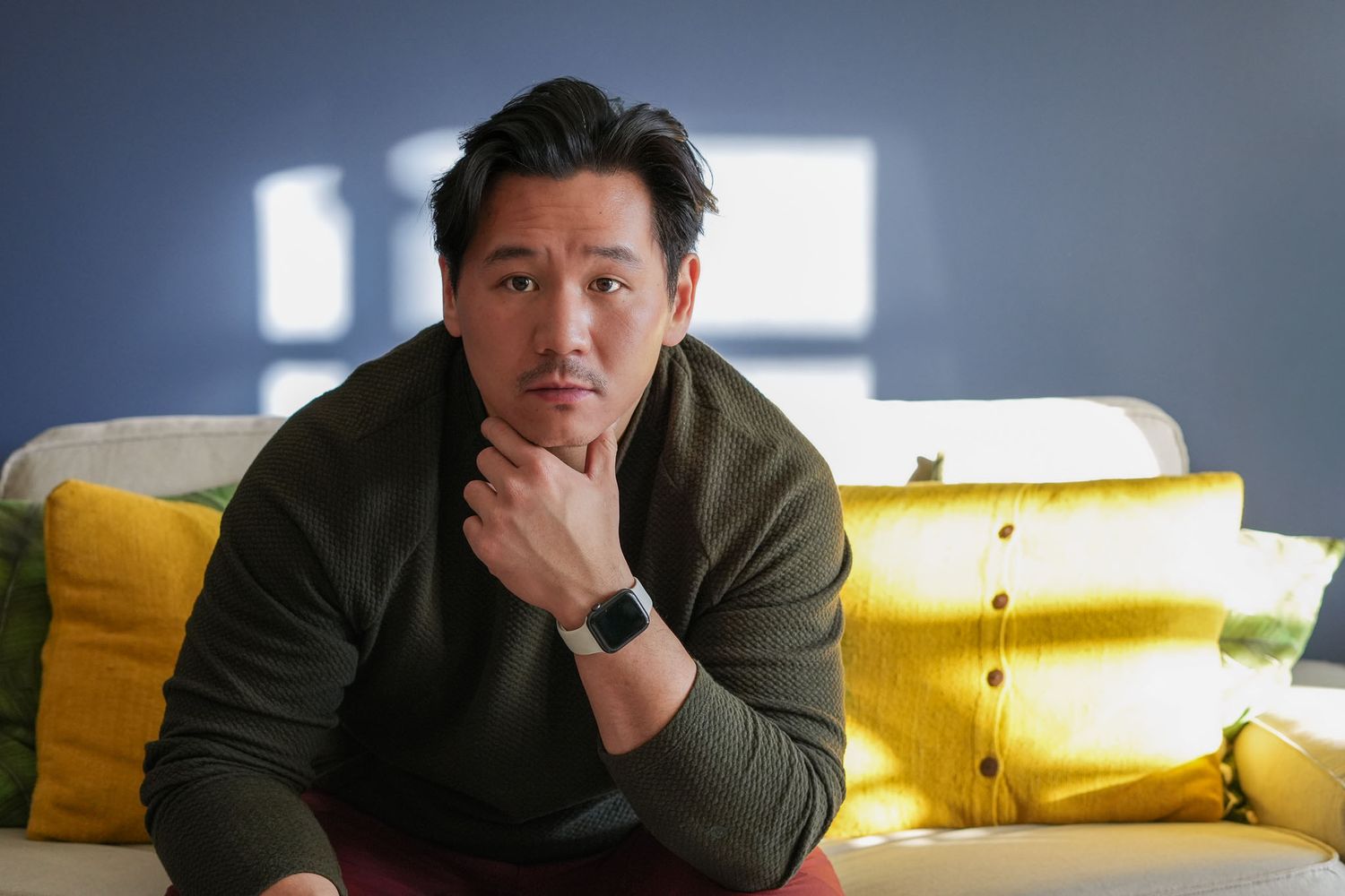 Casual portrait series on a couch with yellow pillows in natural window lighting.