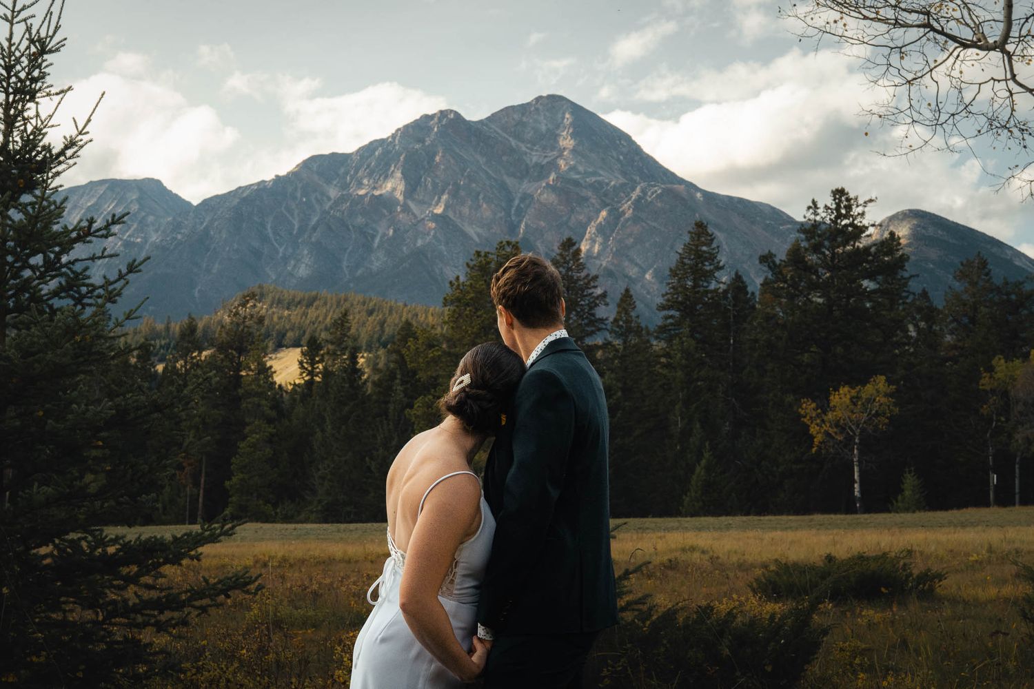 Wedding couple poses against dramatic mountain backdrop during sunset in Jasper, Alberta