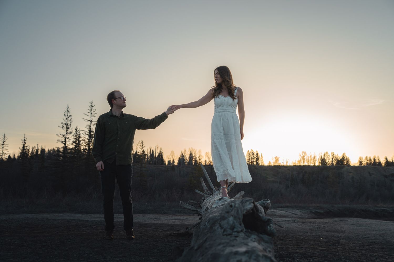 Silhouettes dance against sunrise sky with forest backdrop creating dreamy atmosphere.