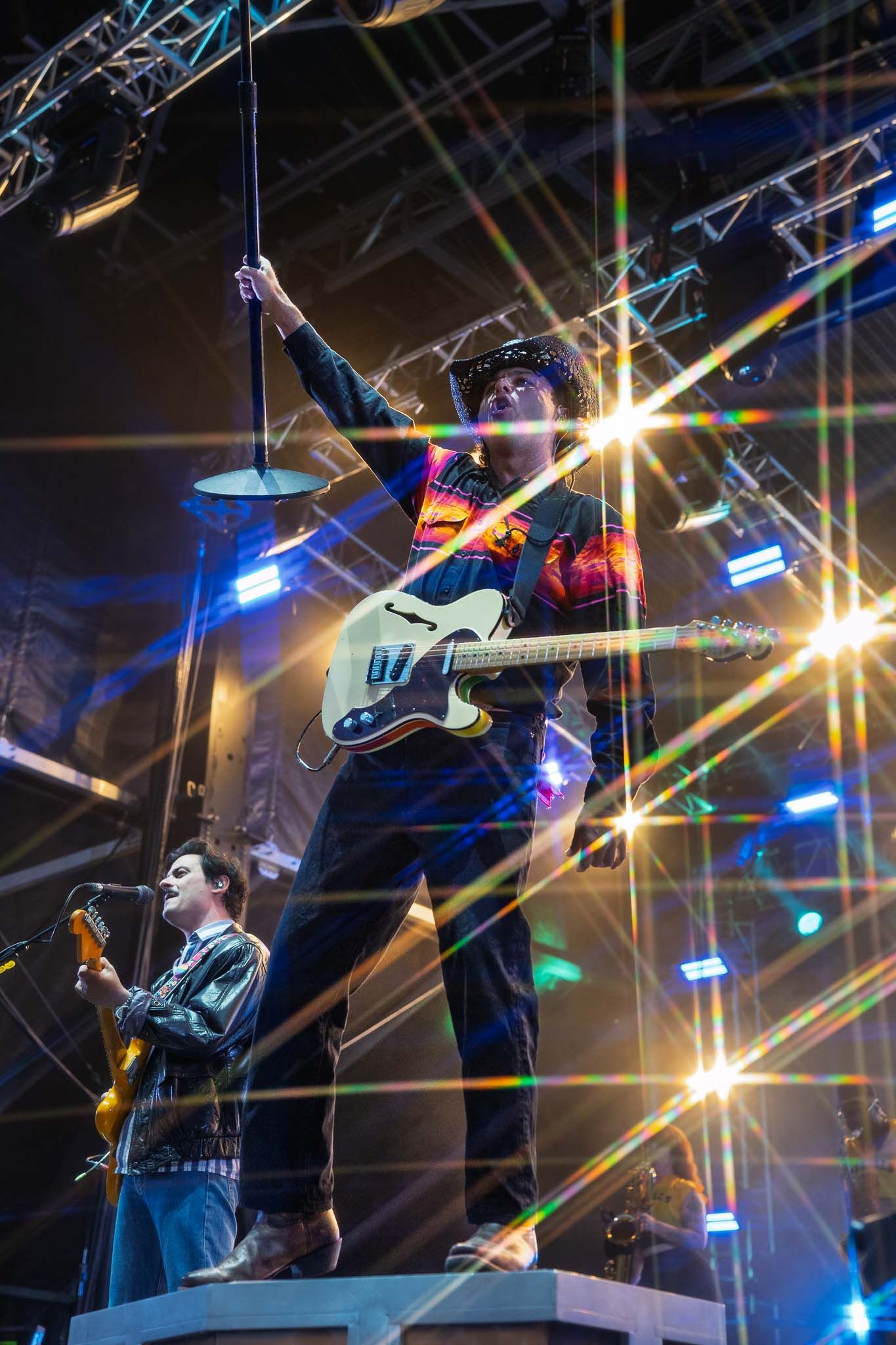 The Arkells perform on stage with dramatic lighting effects and lens flares creating a dynamic concert atmosphere.