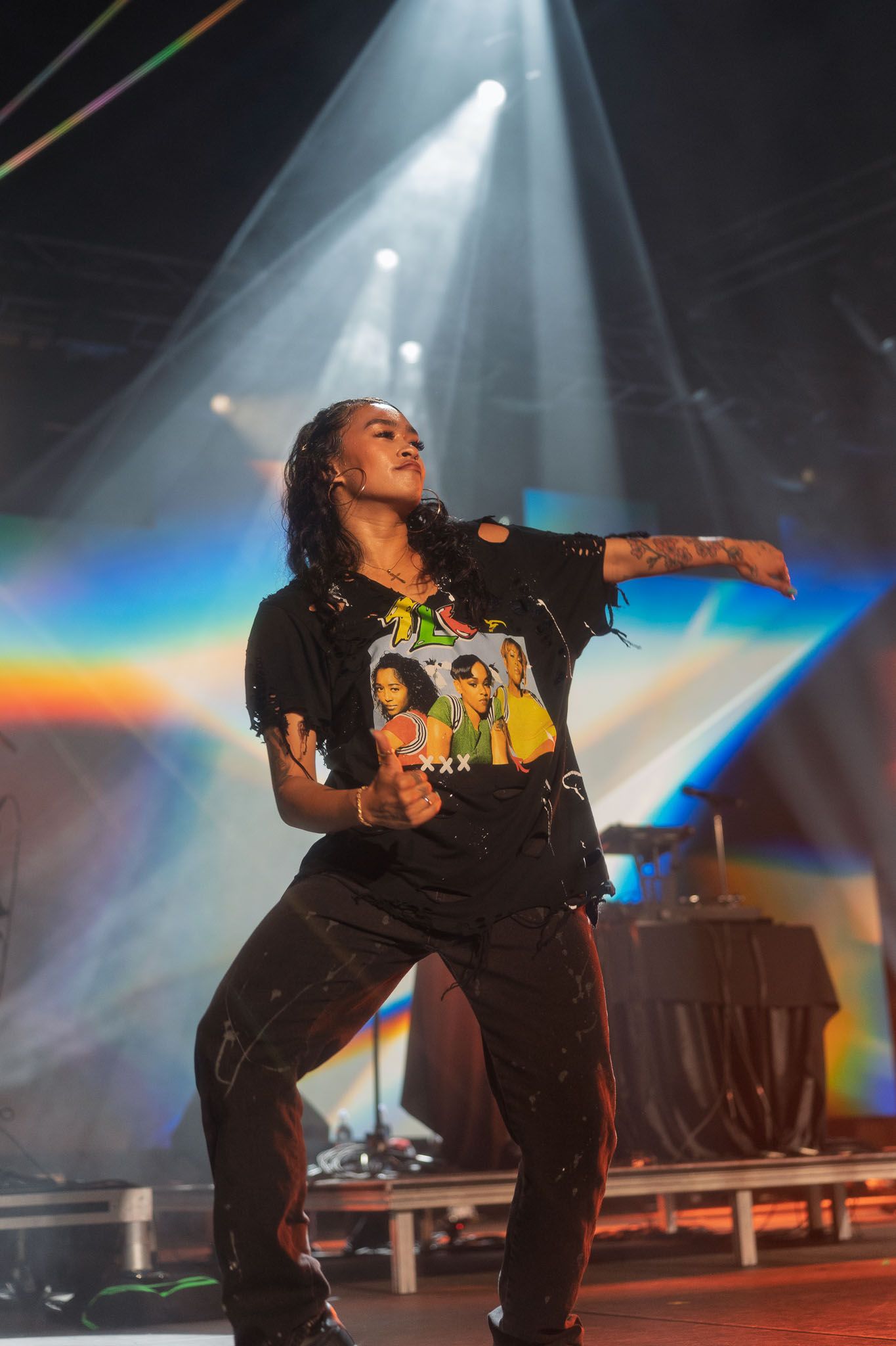 Performer in black outfit dancing on stage with rainbow lighting effects.