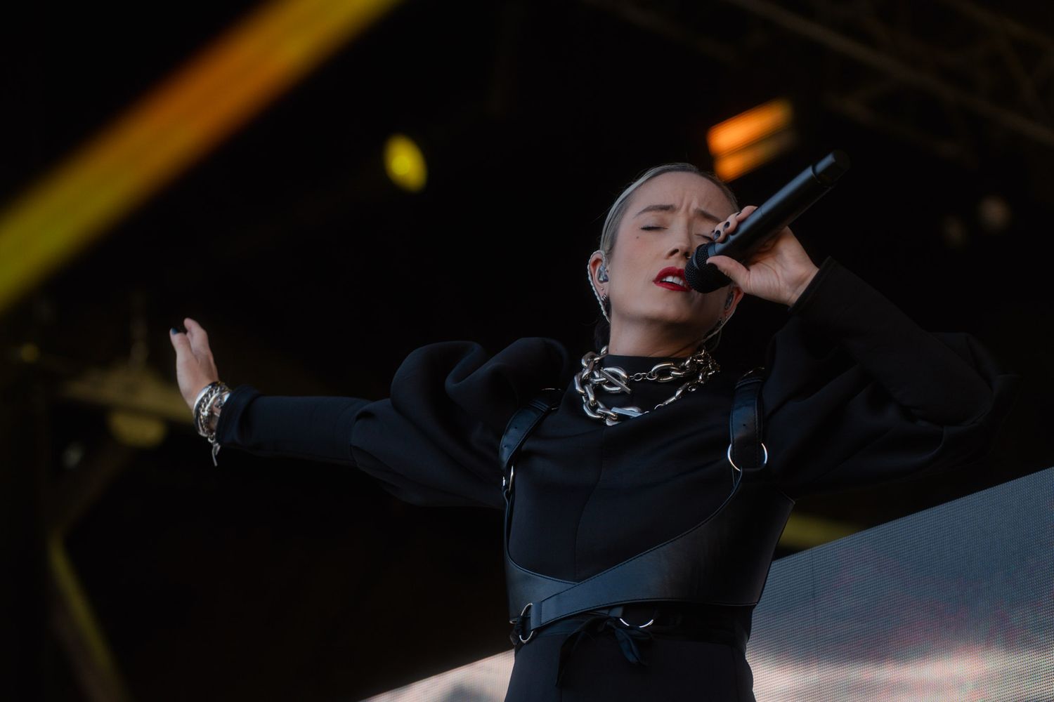 Concert performer Hayla in dark attire gesturing dramatically during stage performance.