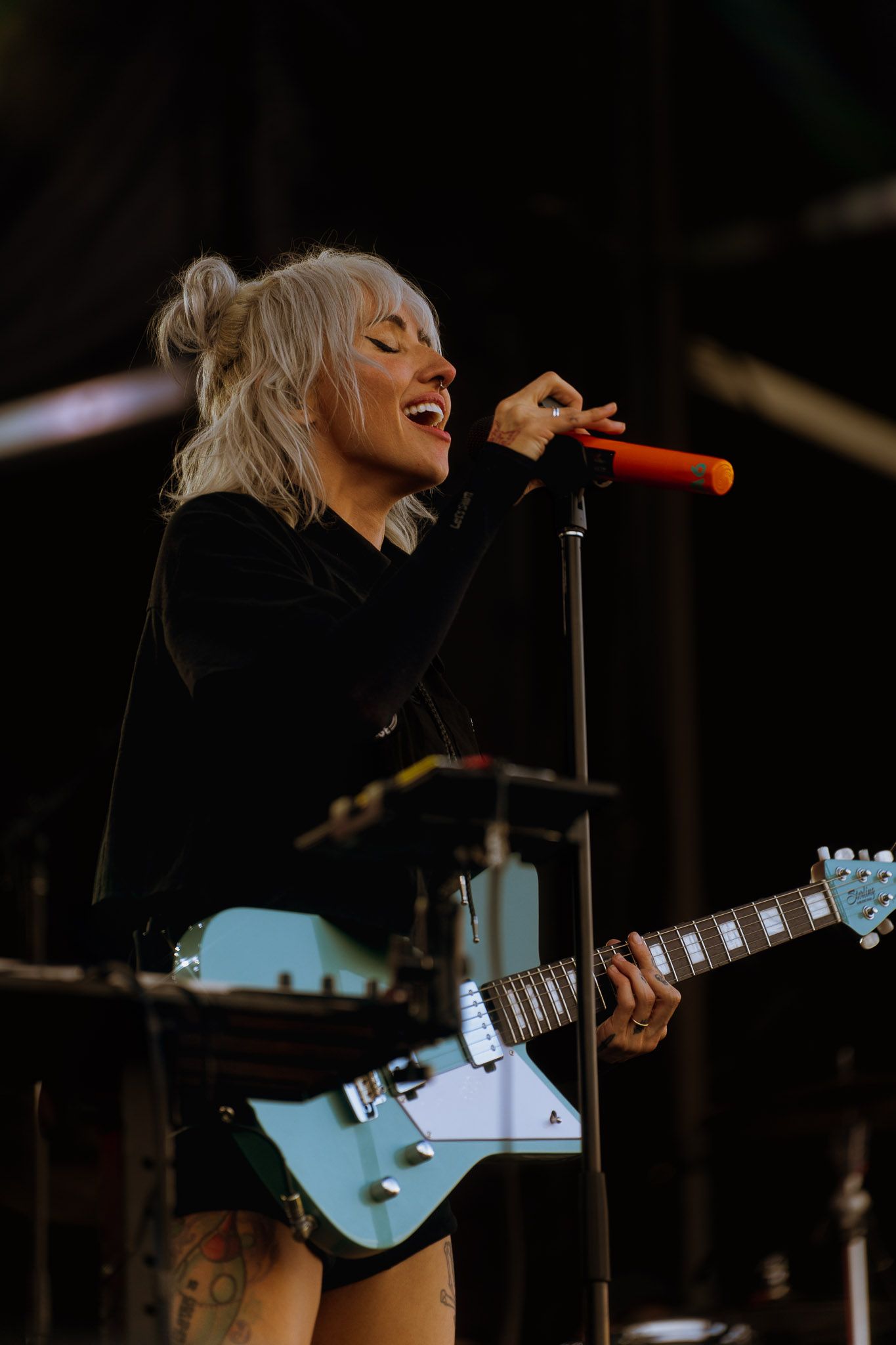 Singer Lights in black outfit performing with light blue electric guitar on dimly lit stage.