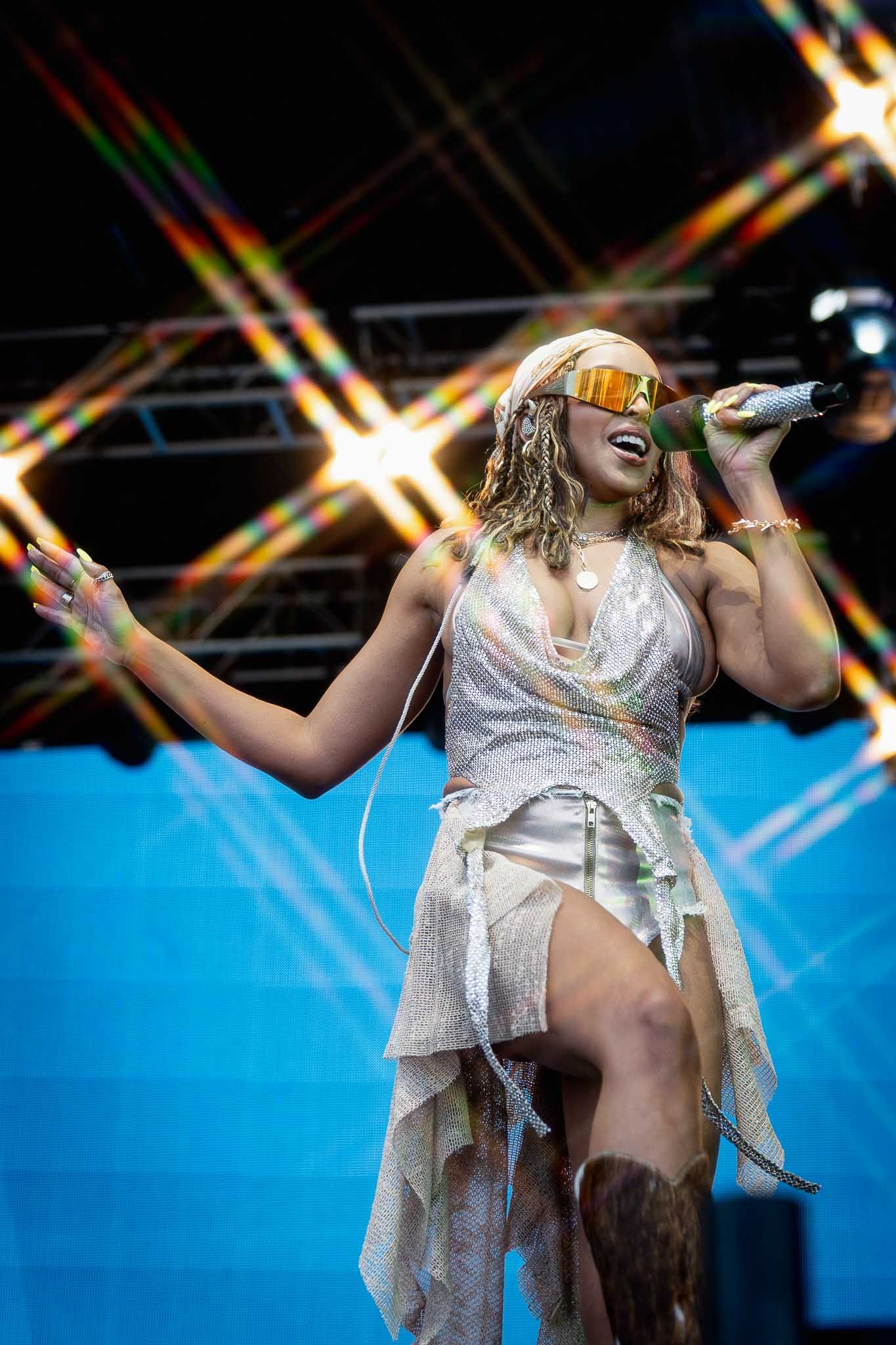 Singer in sparkly silver dress performs energetically on stage with dramatic lighting.
