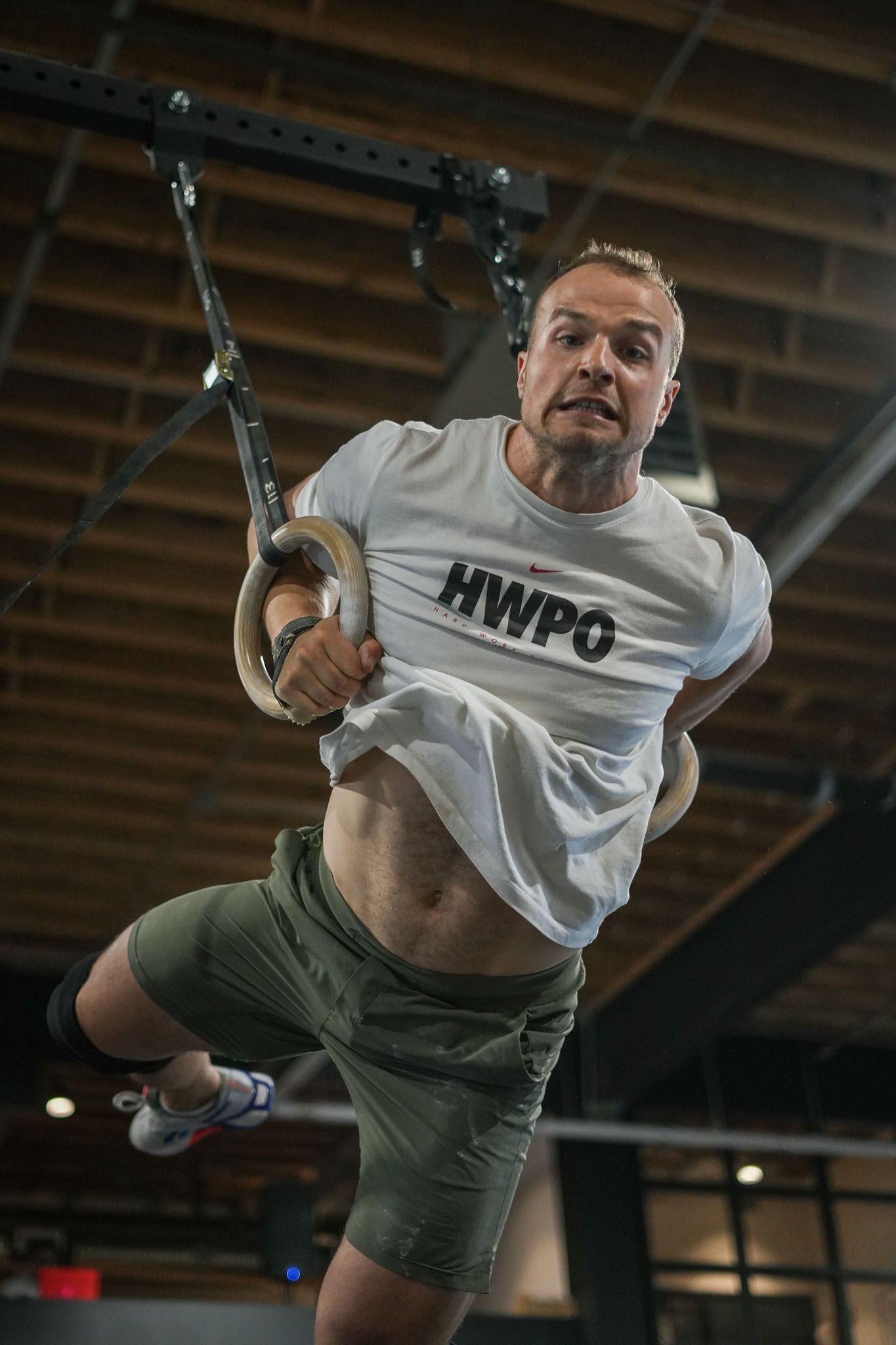 Athletic figure executing strength moves on gymnastics rings in indoor training facility.