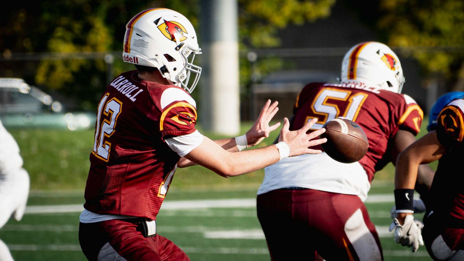 Football action shot showing players from opposing teams in maroon and white uniforms.
