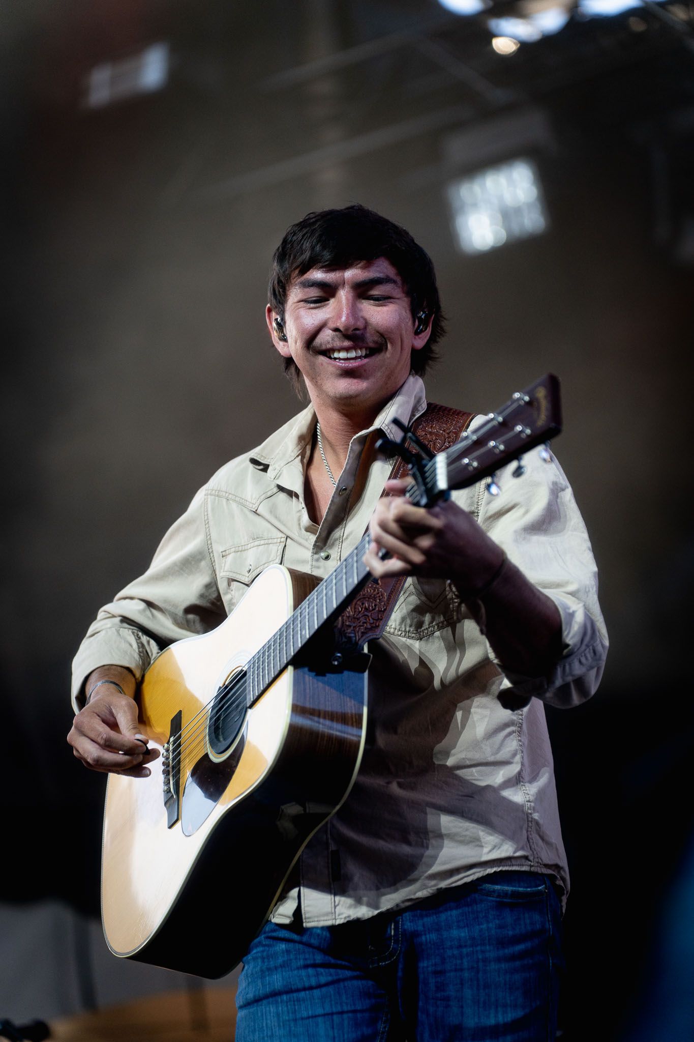 Wyatt Flores strums acoustic guitar during intimate performance with dramatic lighting during the Calgary Stampede