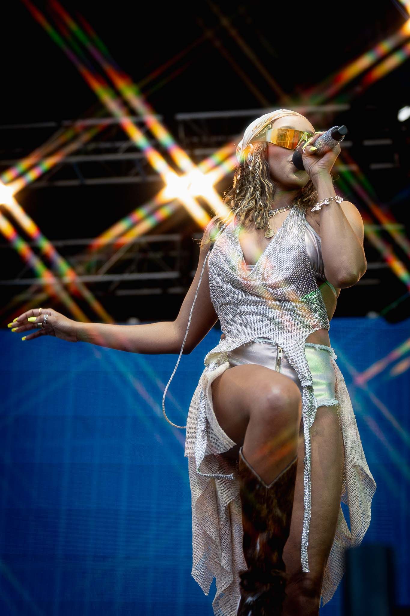 Performer in white sequined outfit dances energetically on stage with dramatic lighting effects.