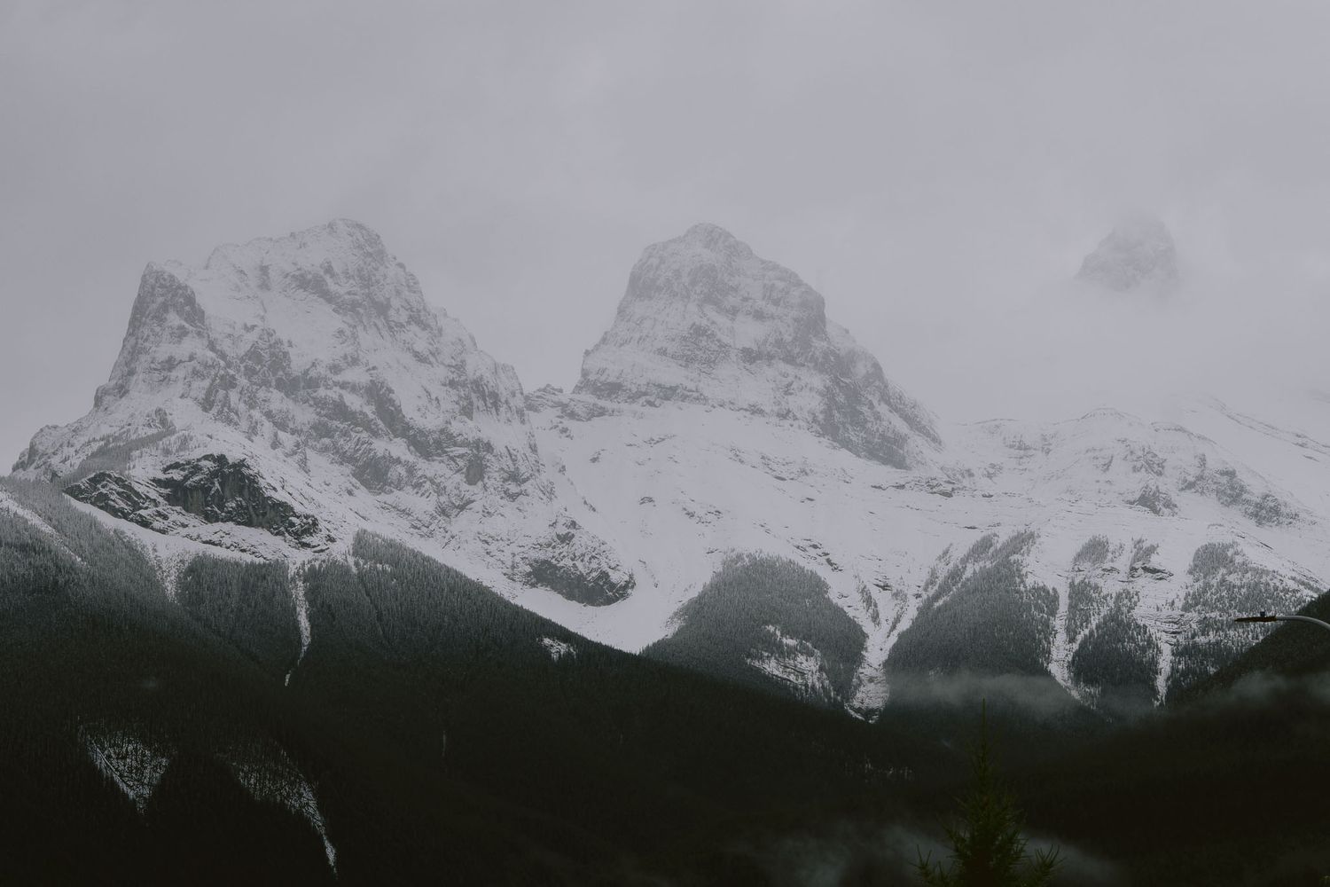Snow-capped mountain peaks stretch across a misty grey horizon in dramatic panorama in Canmore Alberta