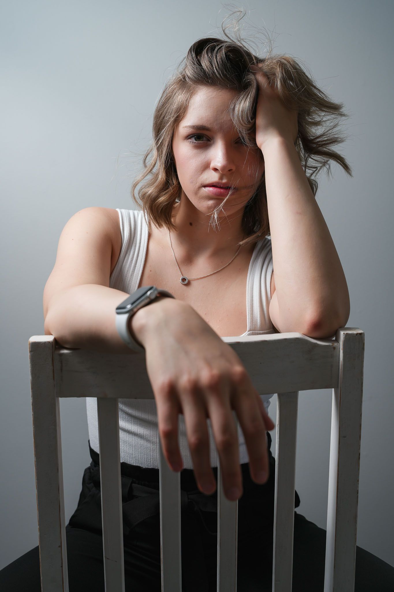 Artistic portrait series showing someone leaning on a white chair against a gray background.