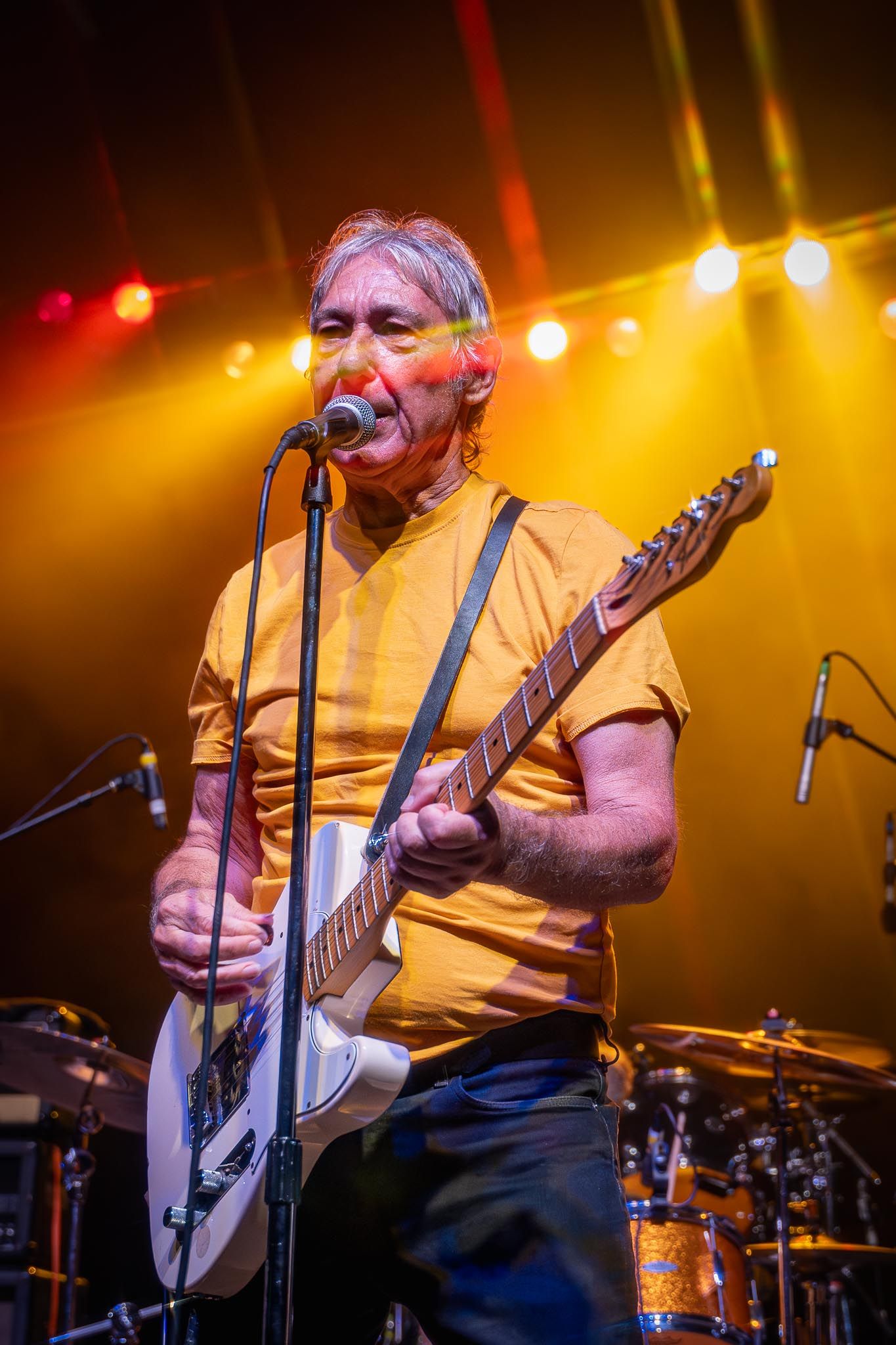 Concert performer singing and playing guitar under warm yellow stage lighting.