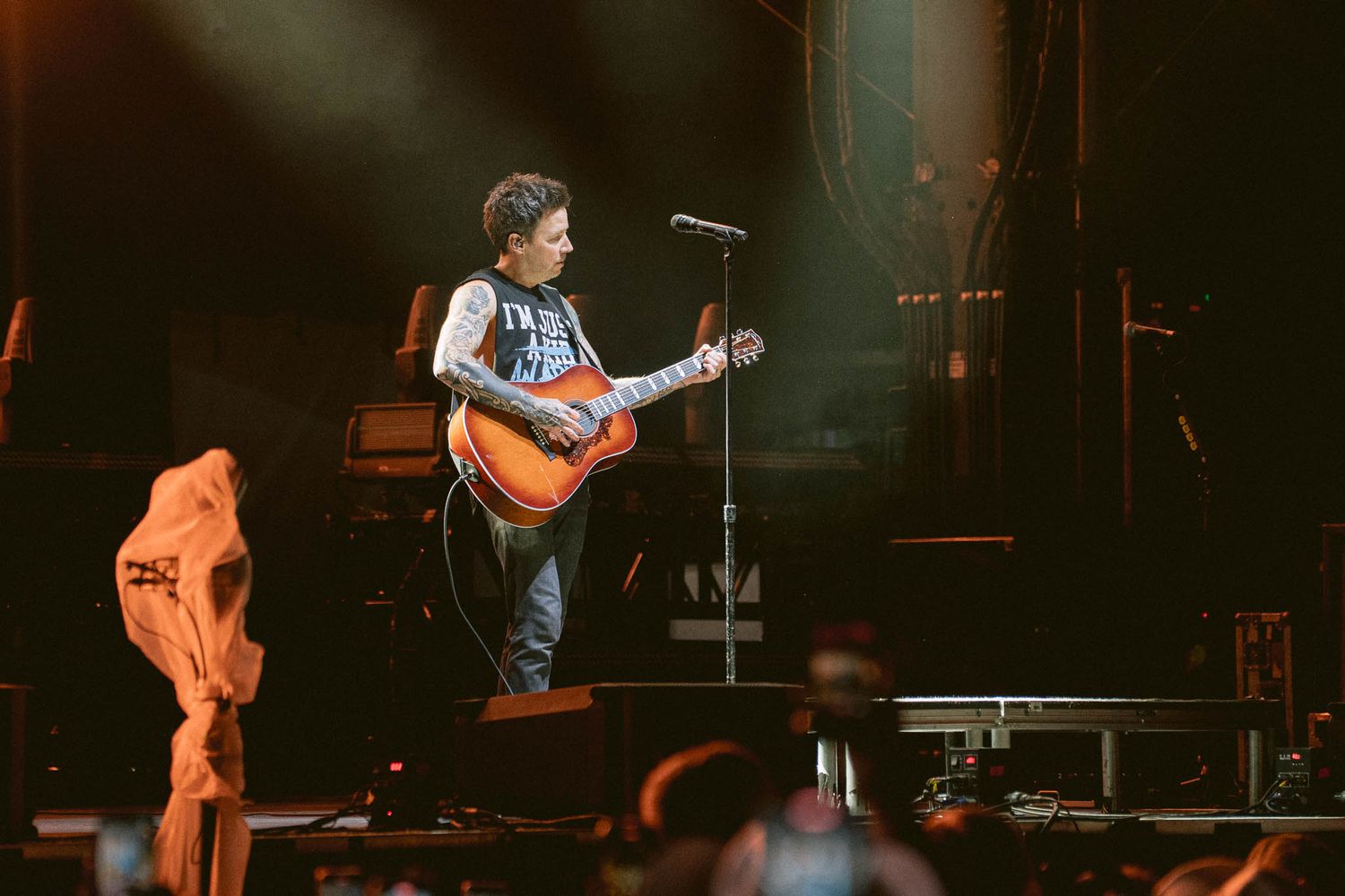 Guitar player performing on stage with orange lighting and amplifiers in background.