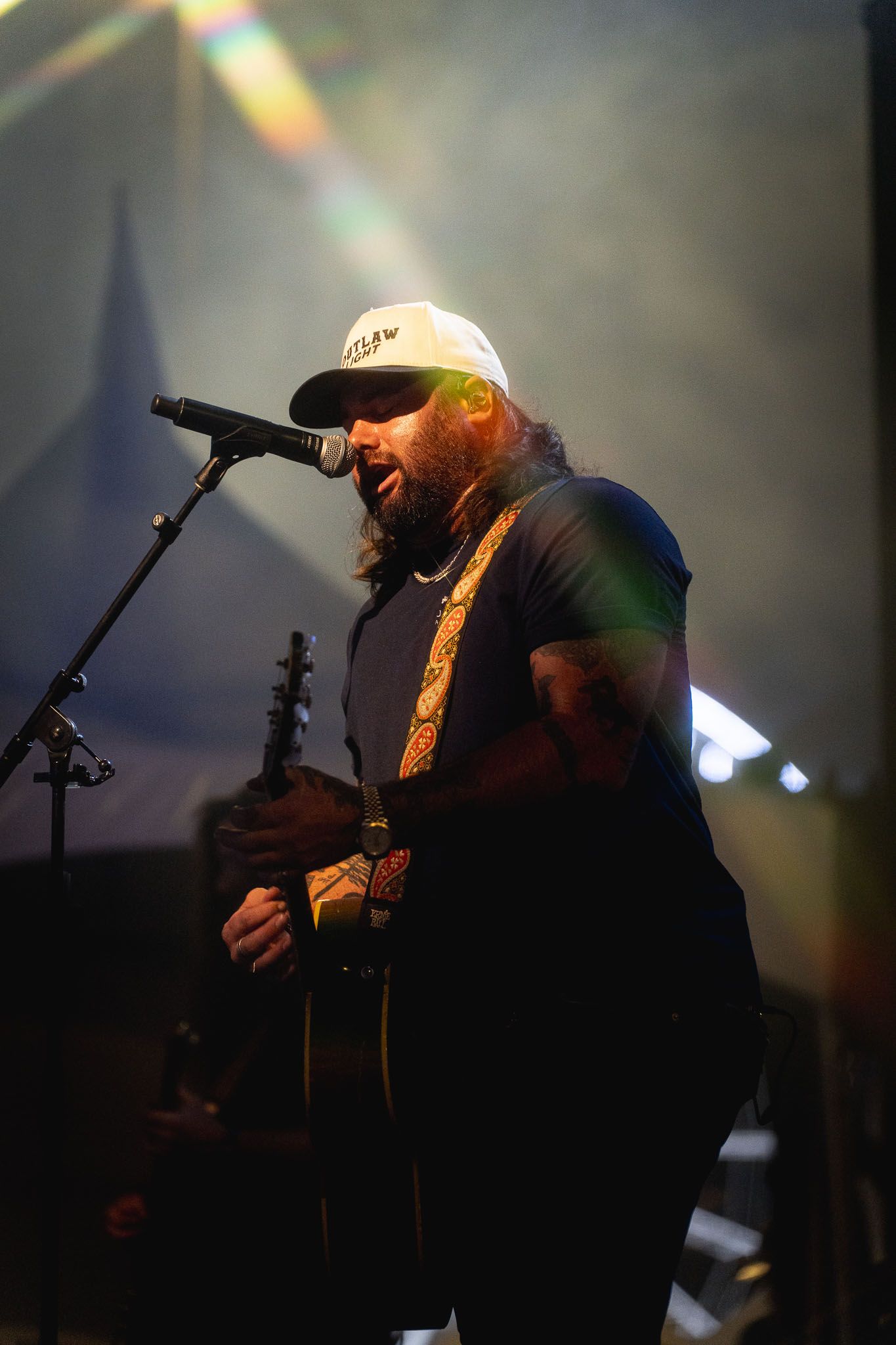 Country performer Koe Wetzel singing into microphone under dramatic stage lighting.