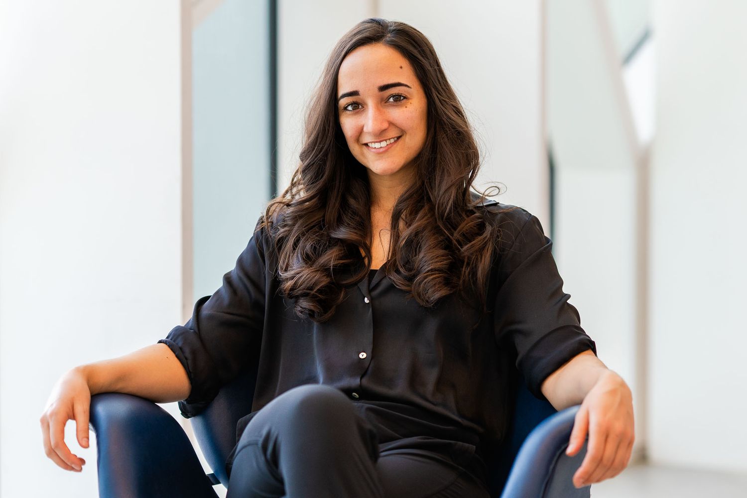 Person in black blazer poses confidently in bright modern office space.