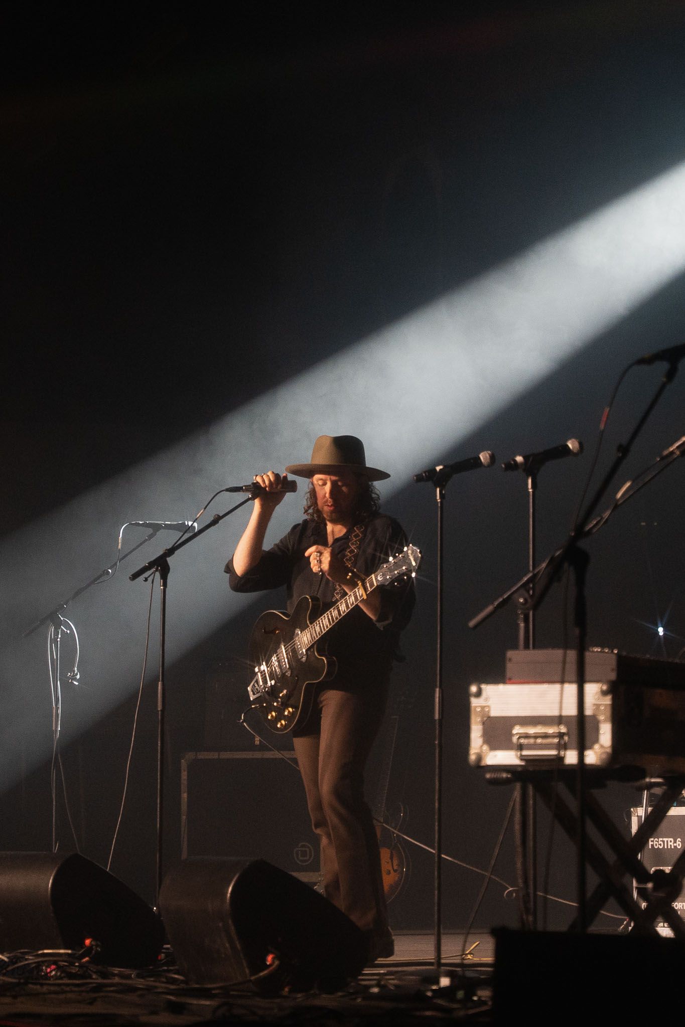 The Paper Kites on stage with guitar under dramatic spotlight beam in dark concert venue.