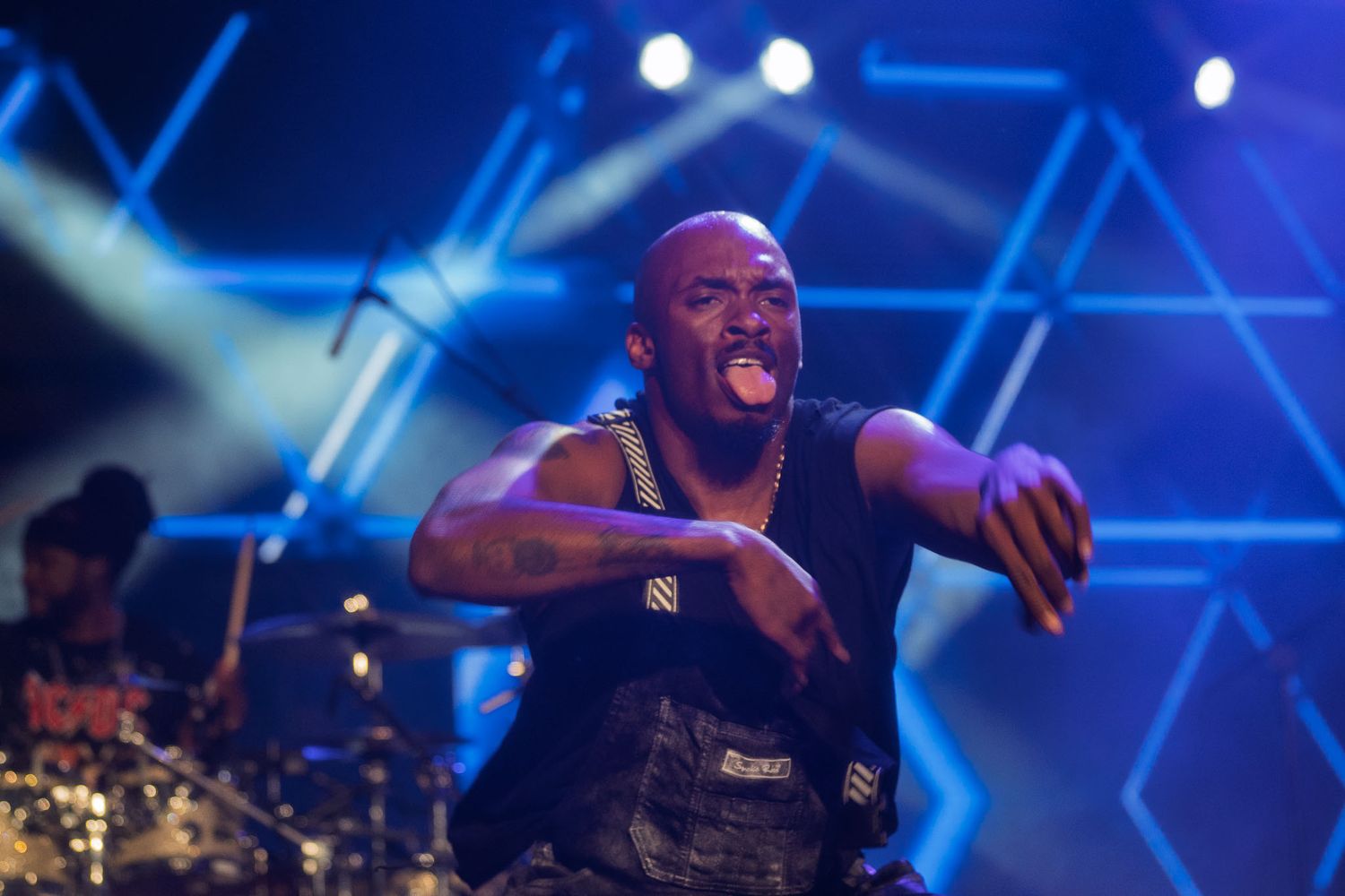 Musicians performing on stage with dramatic blue lighting and concert equipment visible.