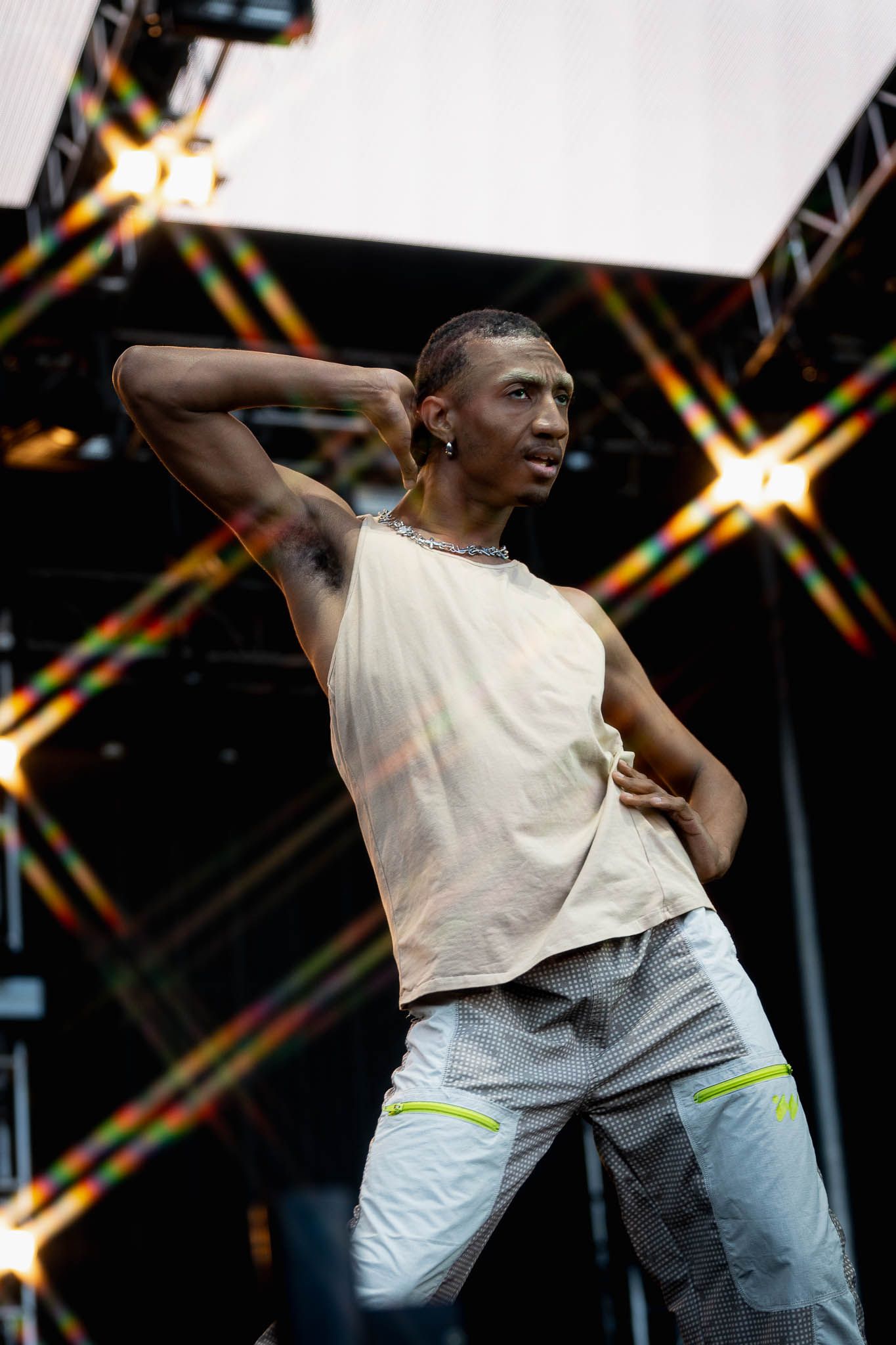 Performer in sleeveless shirt dances expressively against backdrop with starburst lighting effects.