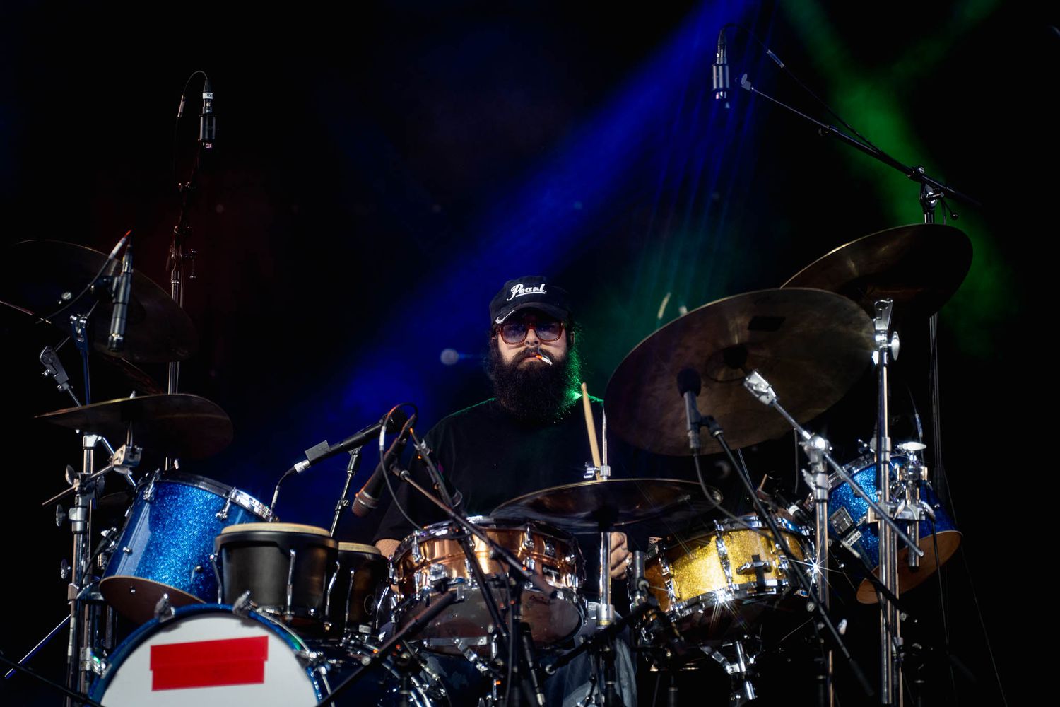 Drummer performs behind drum kit with dramatic blue stage lighting effects.