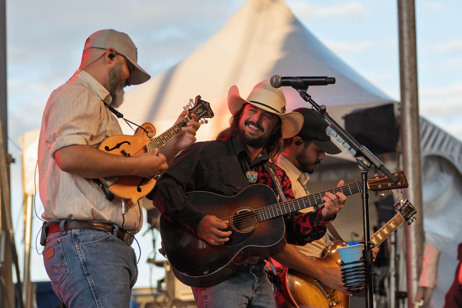 Country musicians playing guitars and fiddles during an outdoor daytime performance.