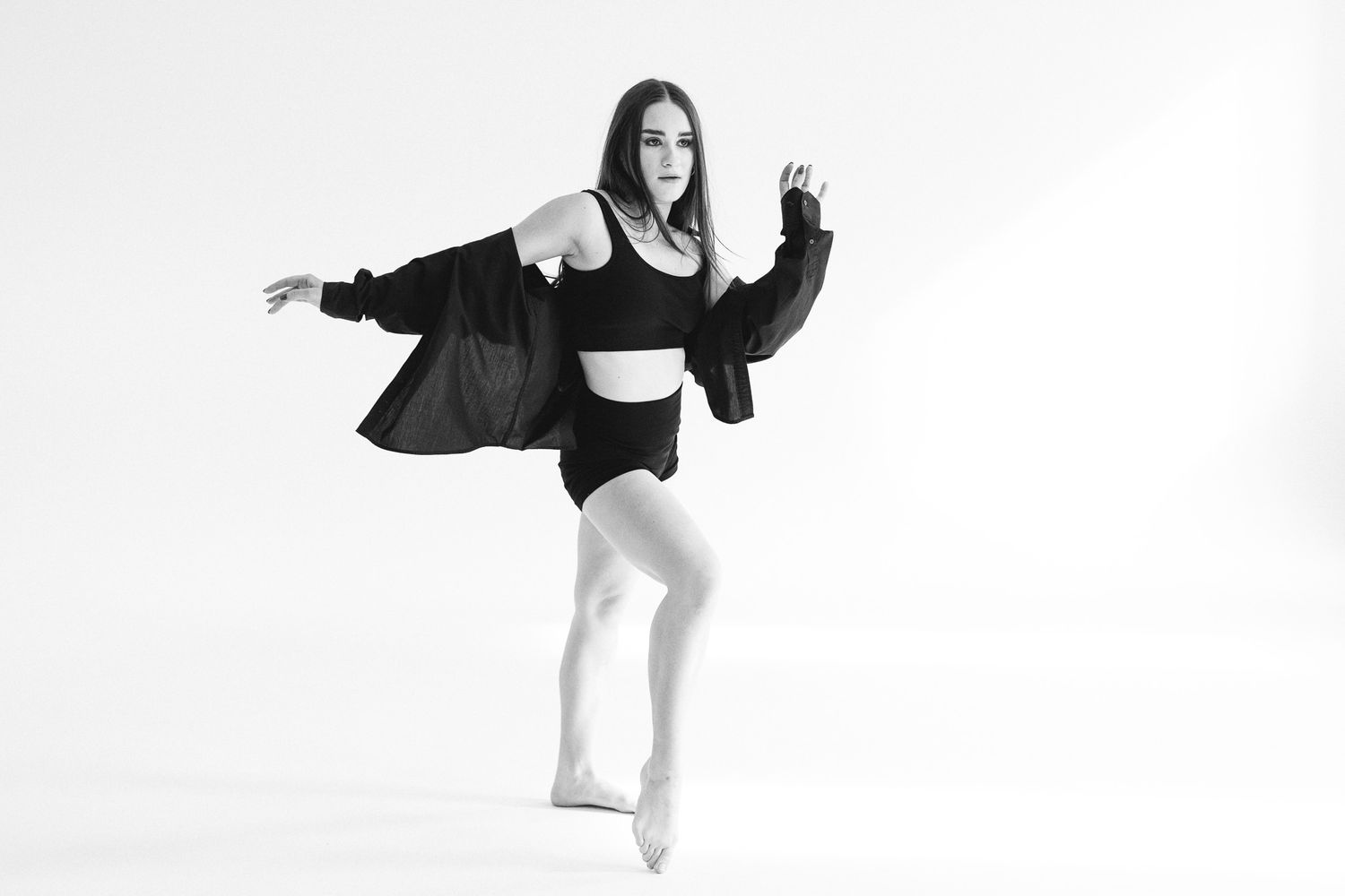 Dancer in black outfit performs dynamic movements against white studio background.