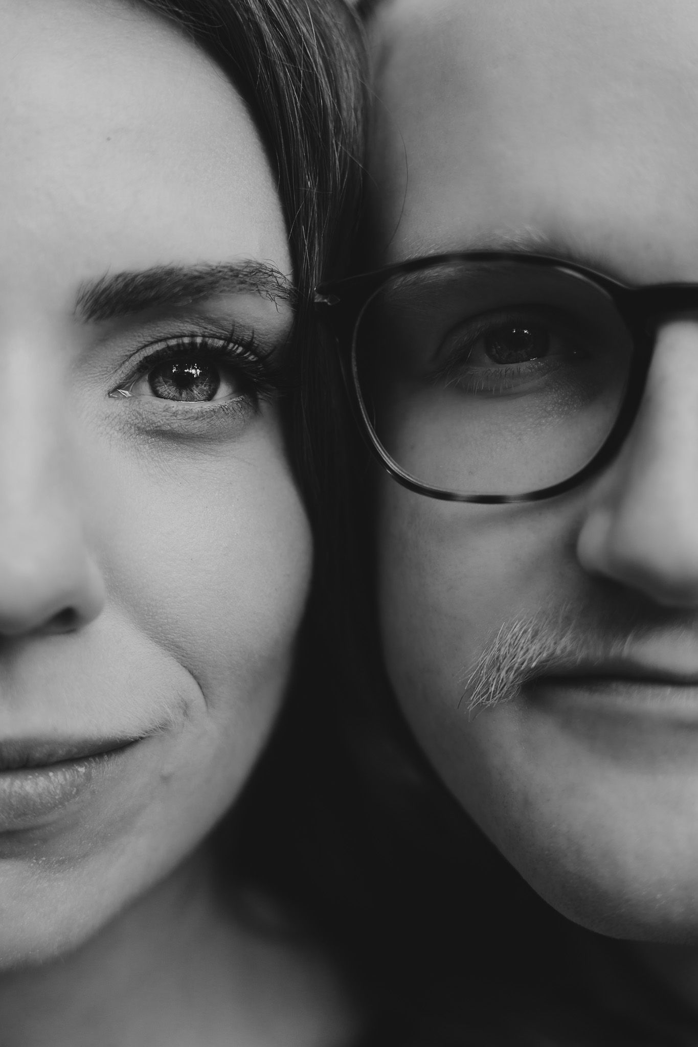 Artistic black and white close-up portrait showing partial faces and one pair of glasses.