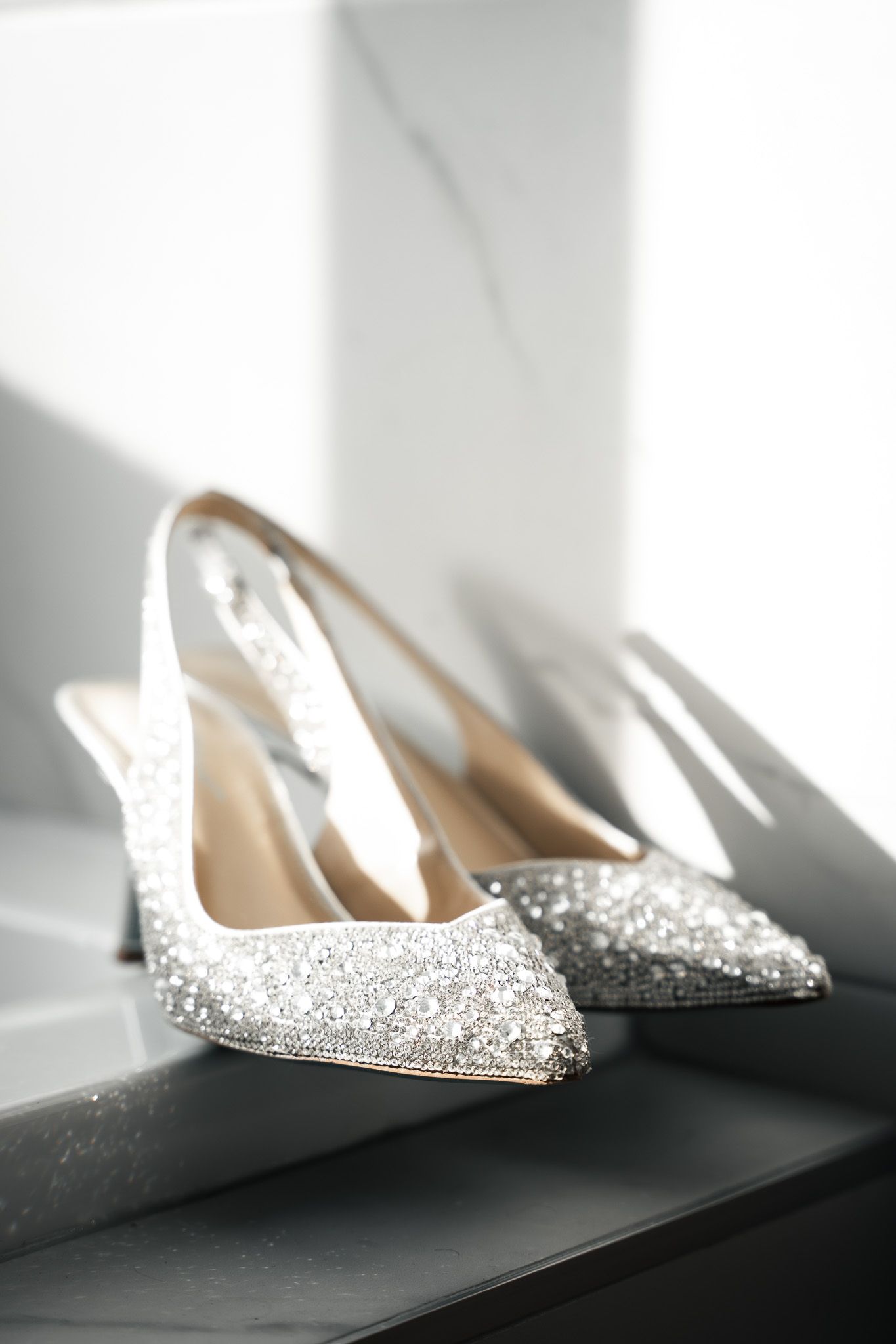 Sparkly bridal shoes catch sunlight through window creating dramatic shadows.