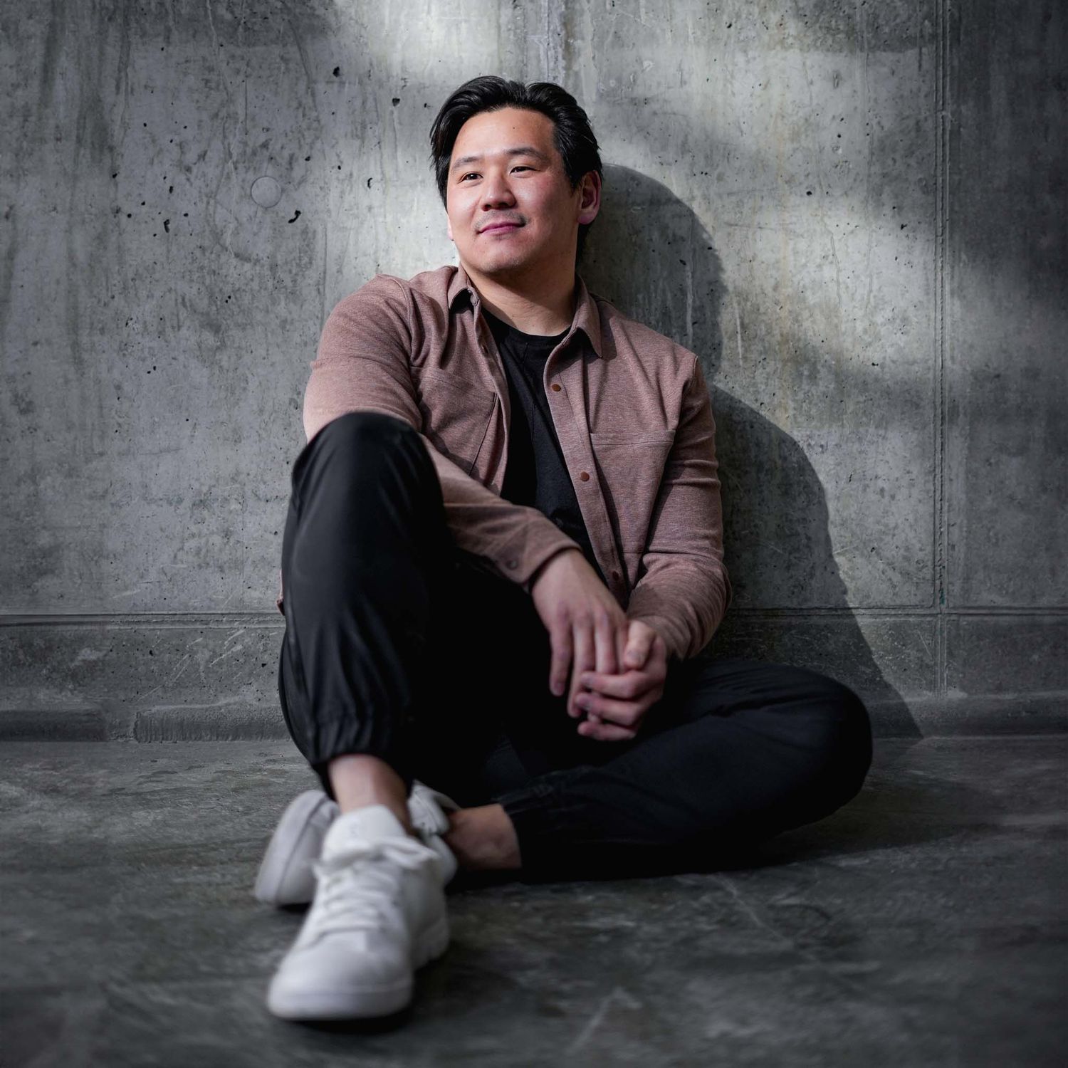 Casual portraits of person in brown jacket lounging on concrete floor with white sneakers.