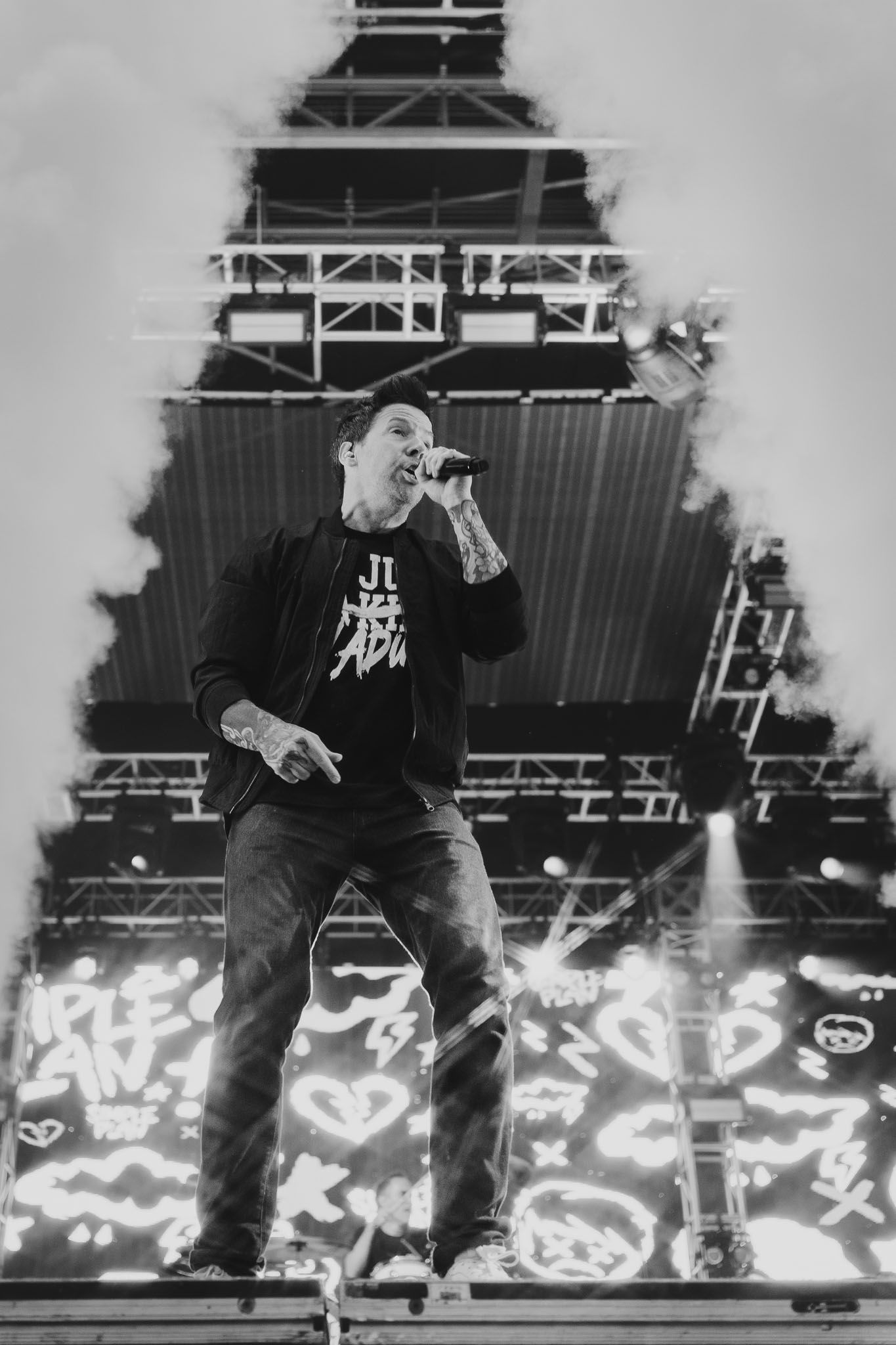 Black and white concert photo showing performer silhouetted against illuminated stage graphics.