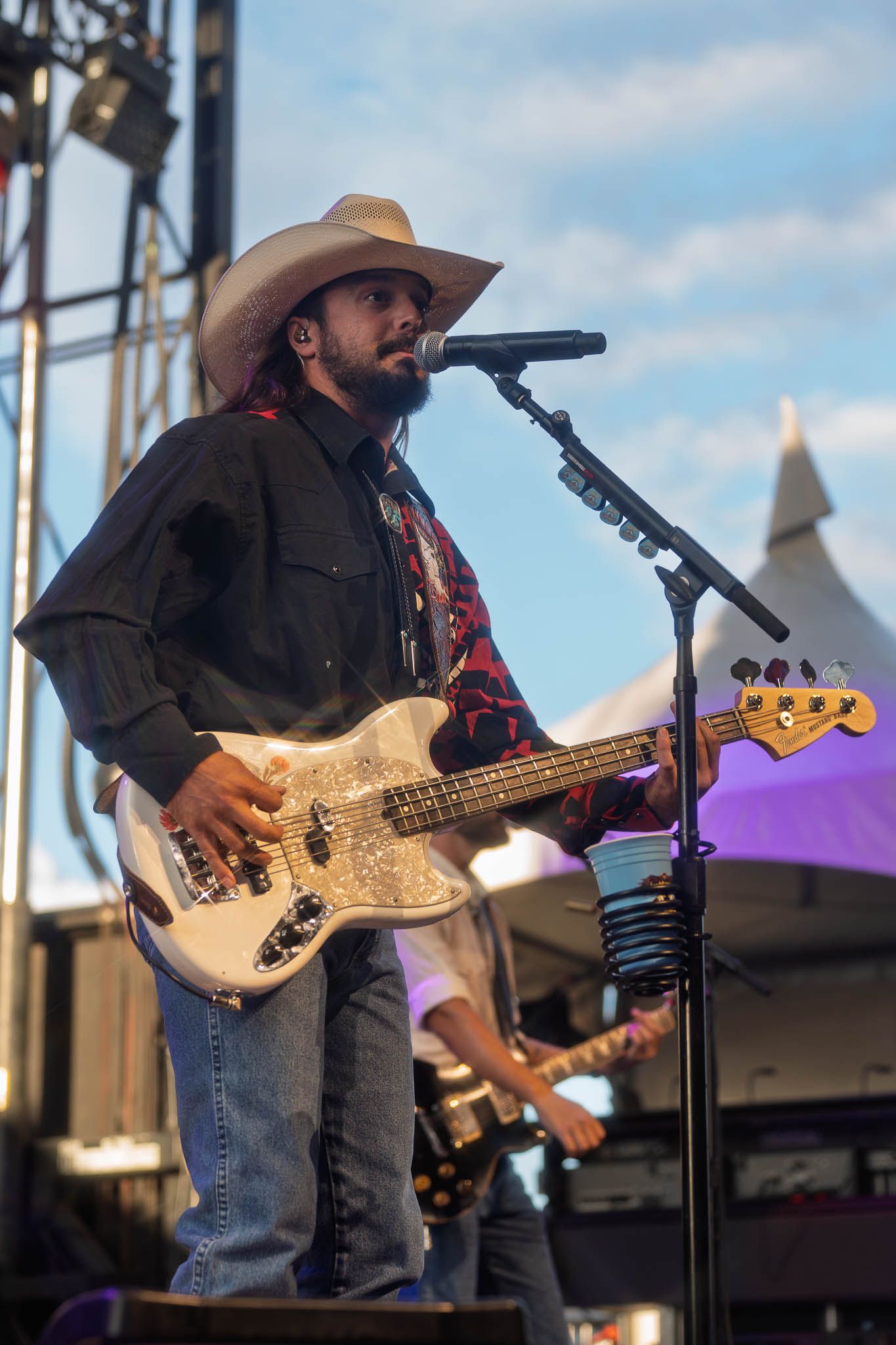 Country musician Ian Munsick with cowboy hats performing with bass guitars on outdoor festival stage.