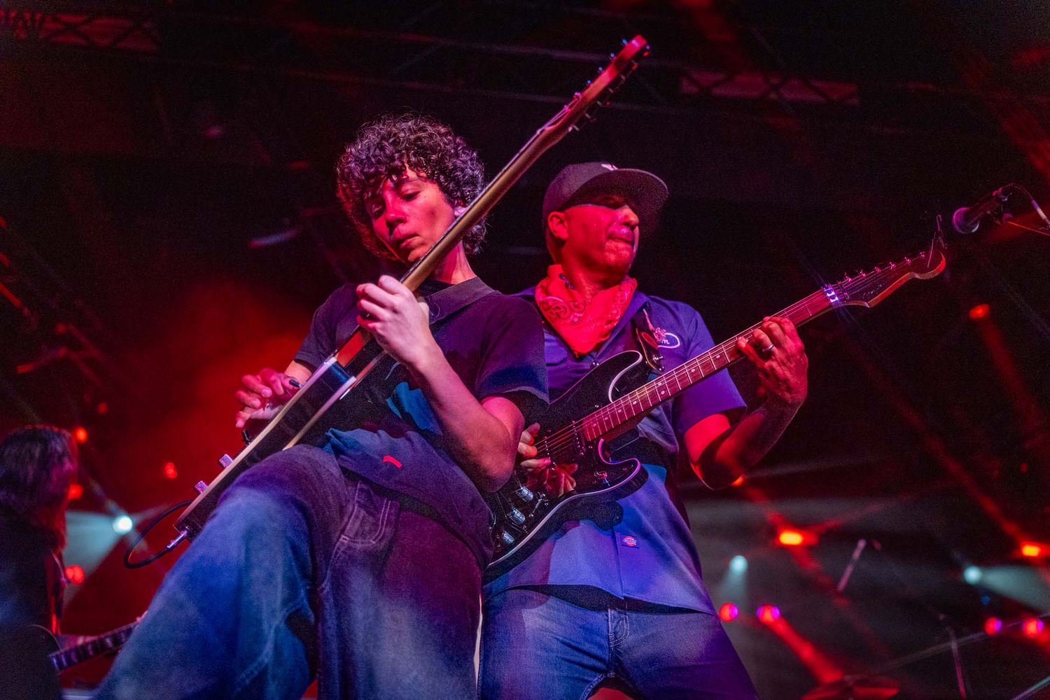 Tom Morello and son Roman Morello play guitars under vibrant blue and red stage lighting during an intense live show.