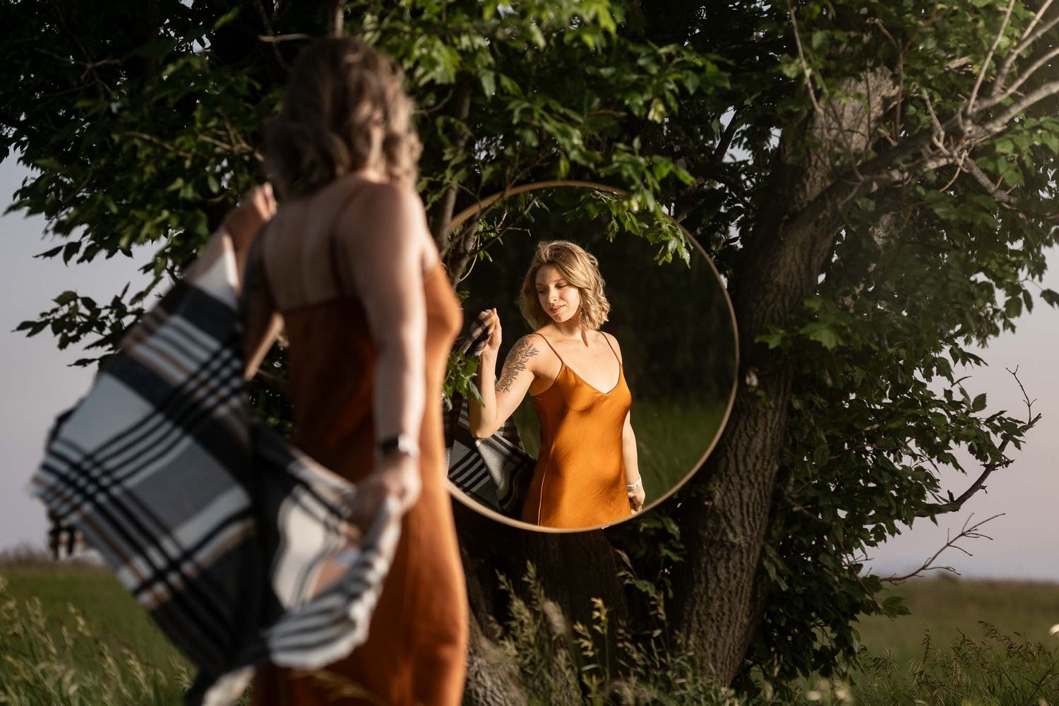 Creative portrait using circular mirror reflection in outdoor natural setting.