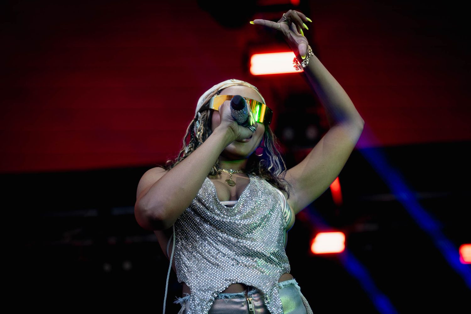 Performer in silver costume and sunglasses dances energetically on stage with dramatic lighting effects.
