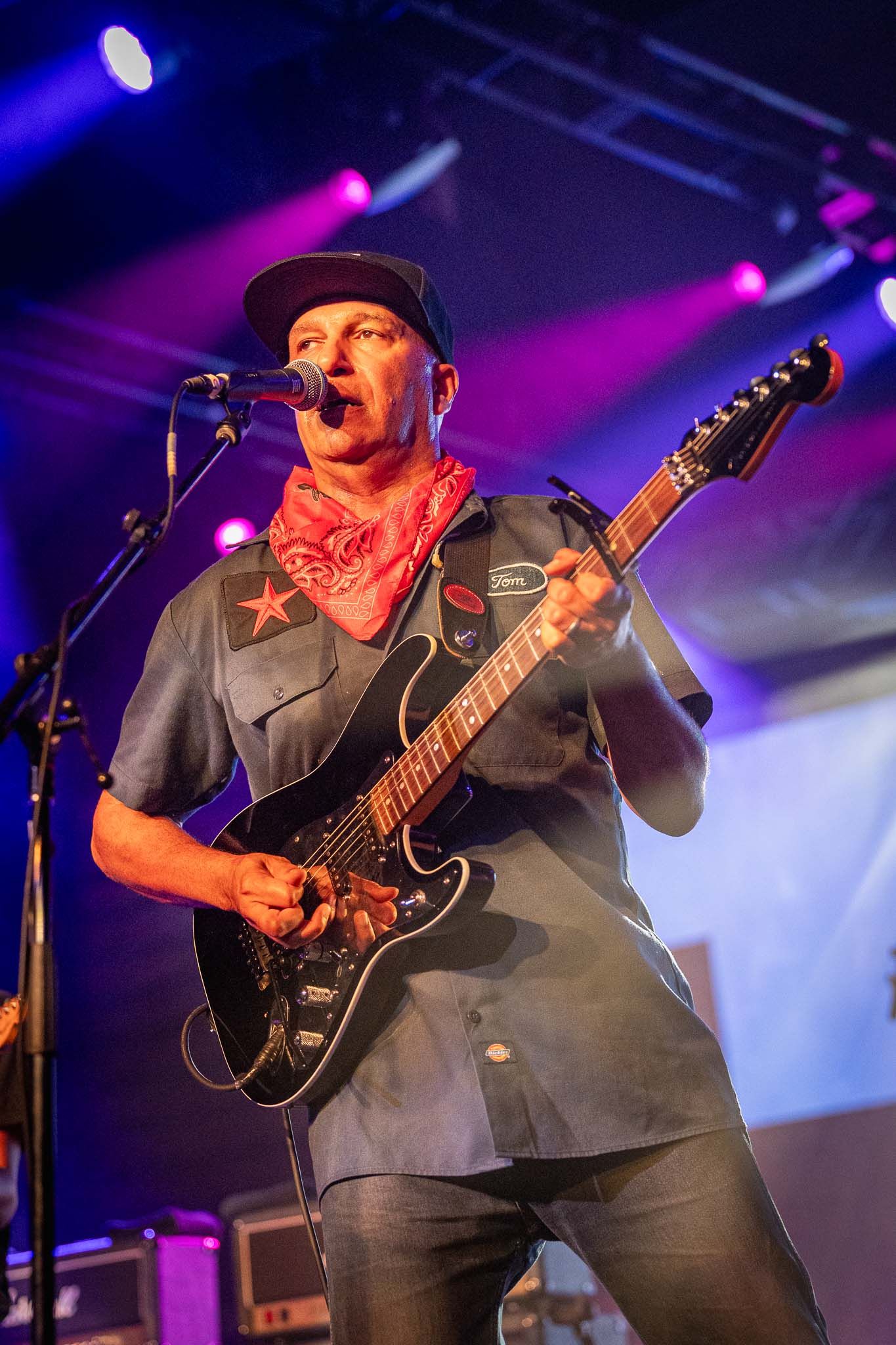 Tom Morello performing on stage with vibrant purple and blue lighting.