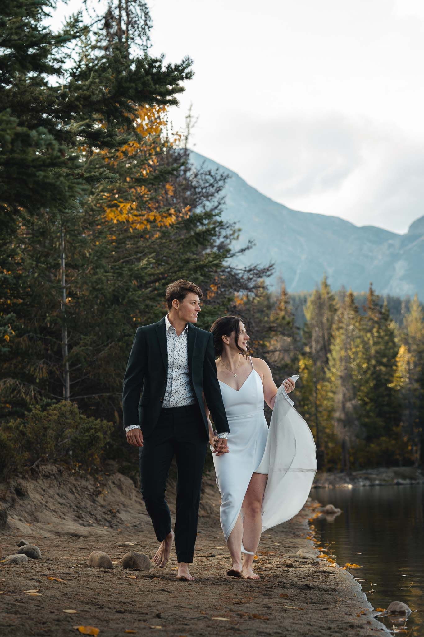 Couple walking along rocky lakeshore with mountain views and fall foliage in Jasper, Alberta by the Fairmont Jasper resort