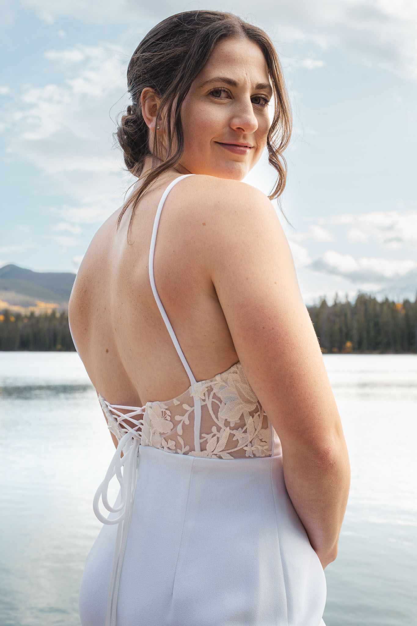 Close-up details of a white wedding dress with delicate lace detailing against a lakeside backdrop.