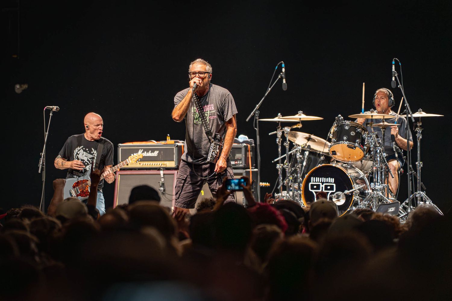 Wide shot of The Descendents band performing on stage with drums and guitar equipment visible.