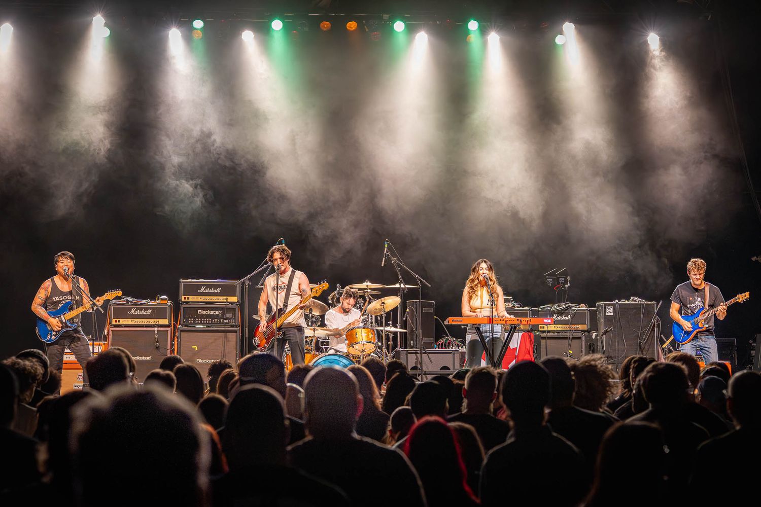 Rock band performs energetically on stage with dramatic lighting and full band setup.