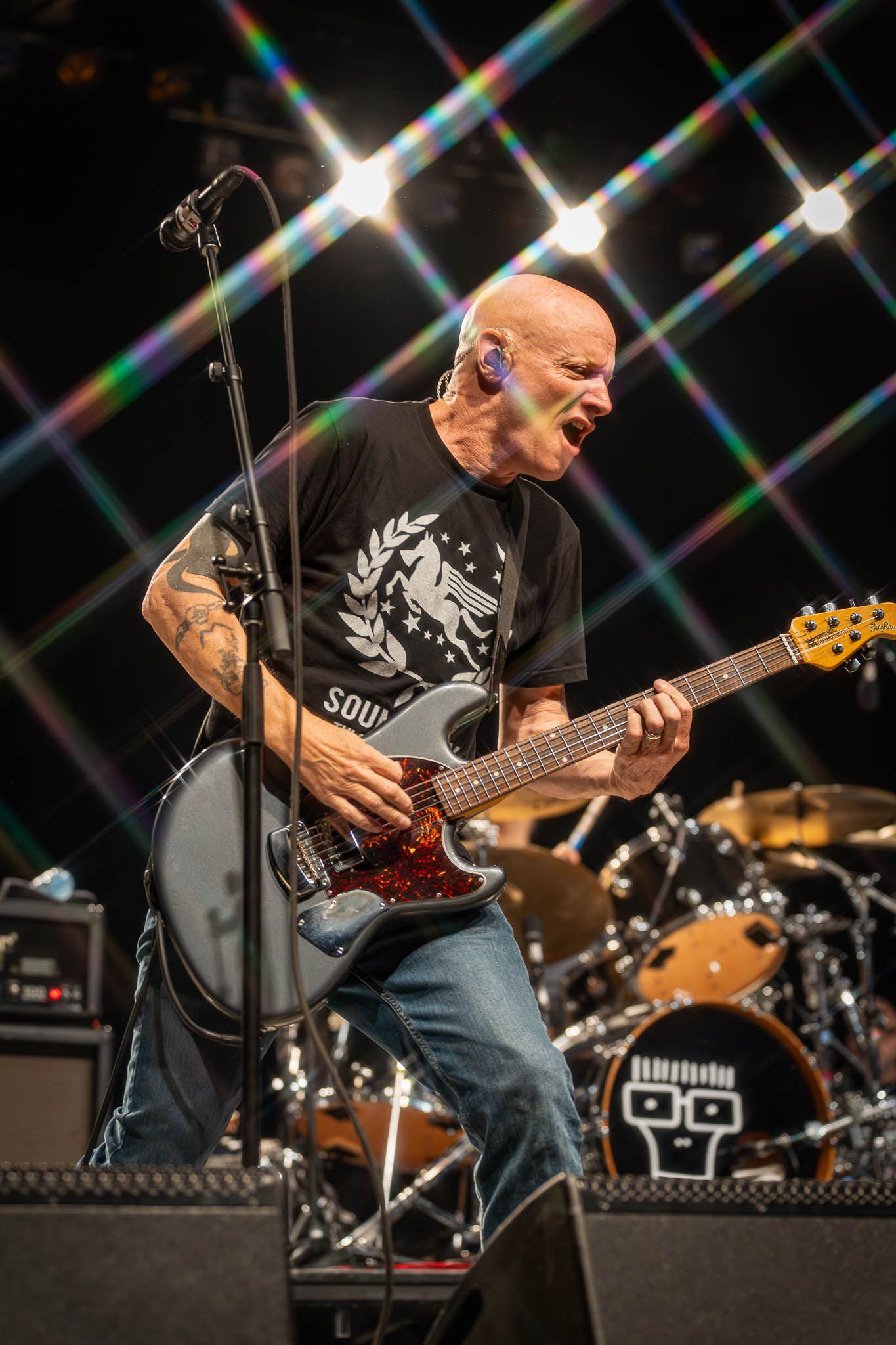 Musician playing electric guitar with dramatic lighting effects creating star patterns in background.