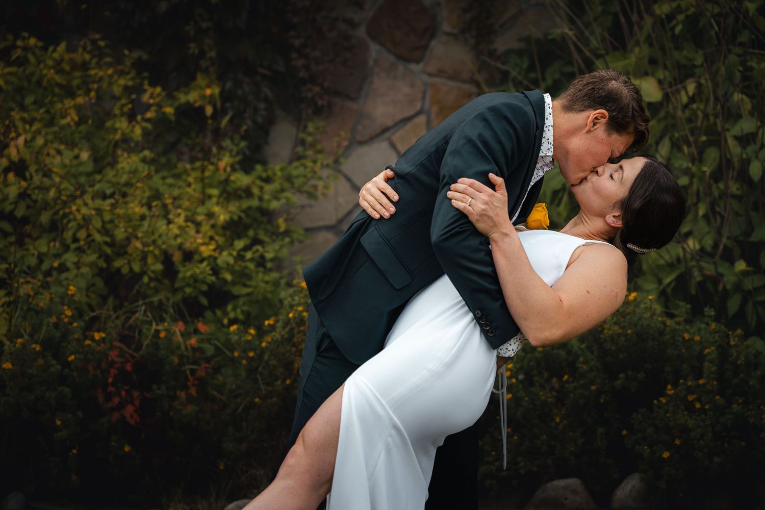 A romantic wedding couple embraces in a wooded outdoor setting during golden hour.