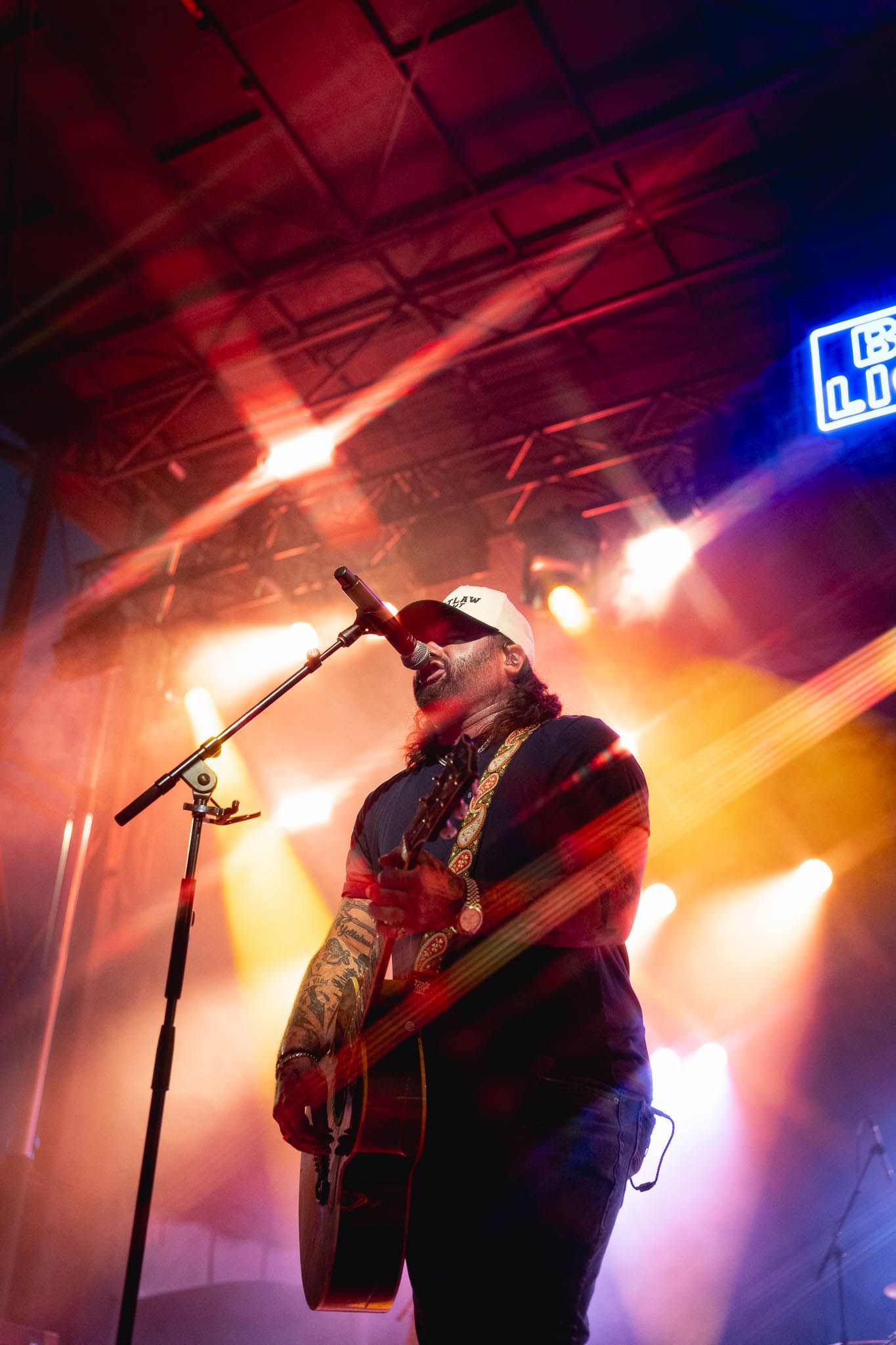 Musician Koe Wetzel perform on stage with dramatic orange and blue lighting creating a silhouetted effect during a concert.