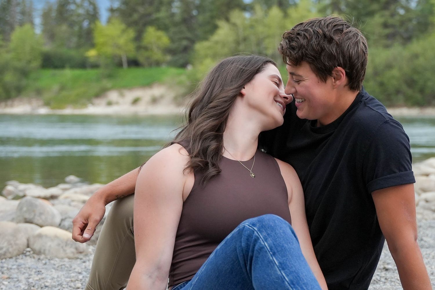 Romantic couple photos by a lakeside with mountains and trees in background.
