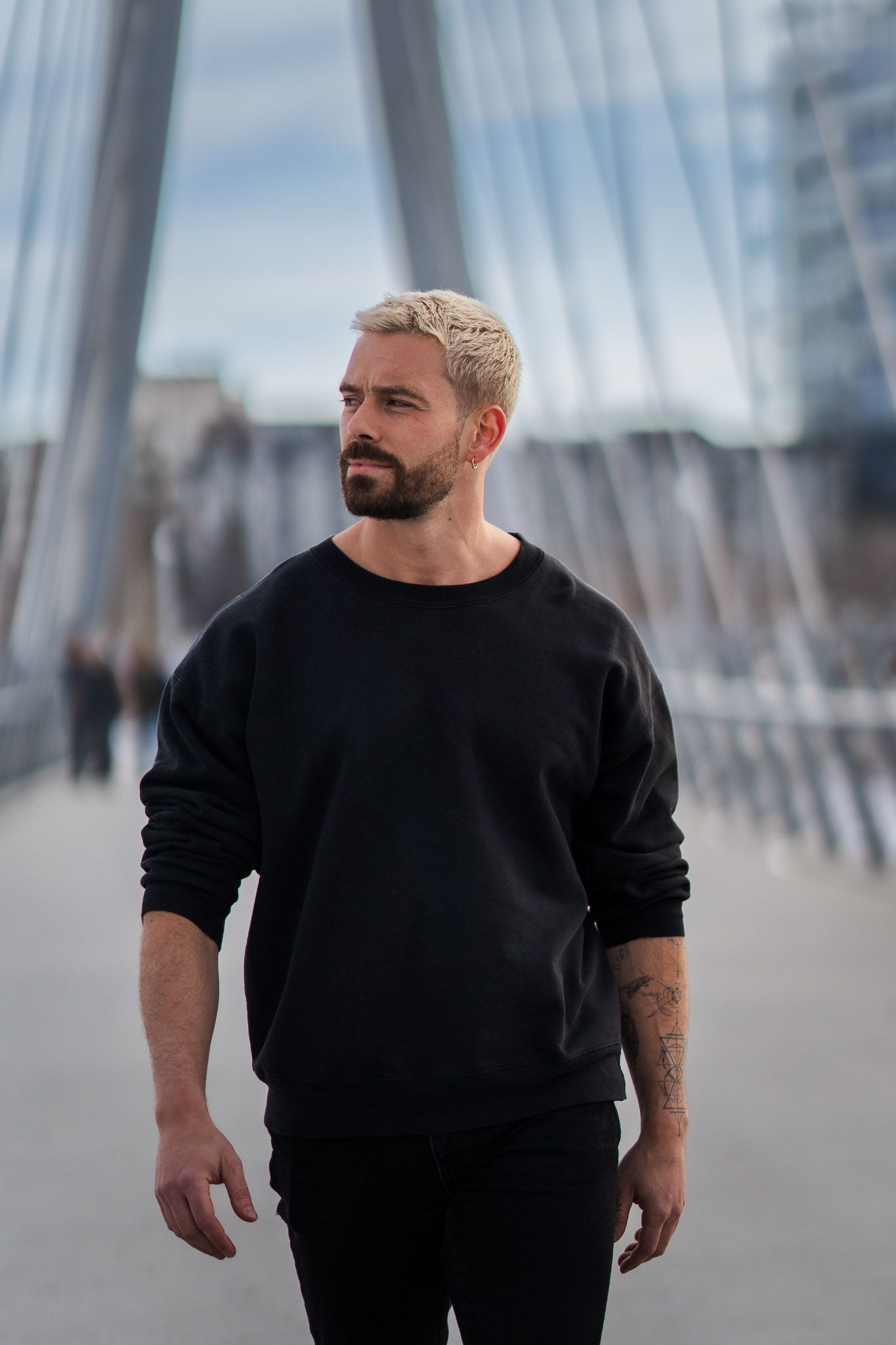 Stylish man in black sweater poses against modern architectural backdrop in urban setting.