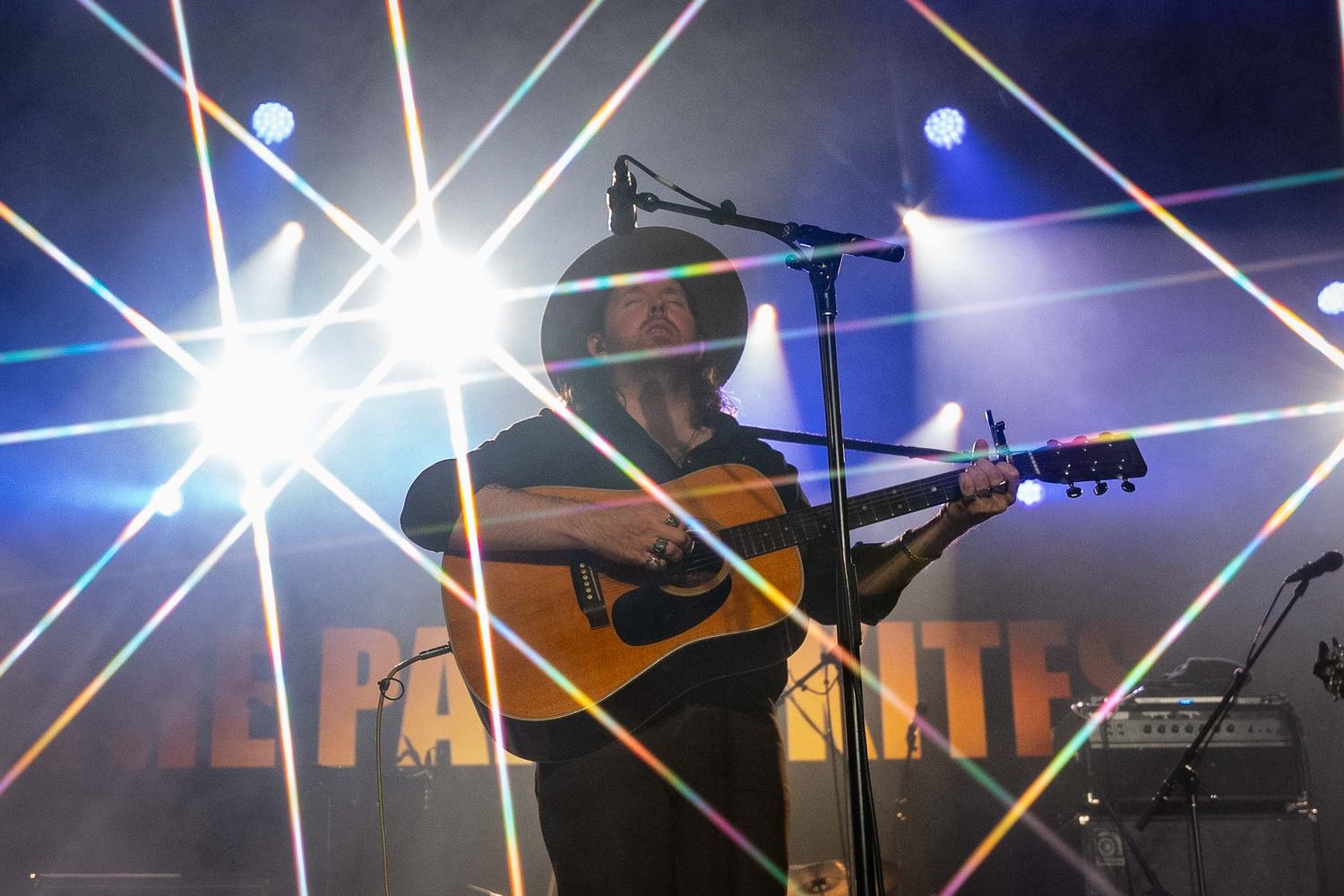The Paper Kites performing on acoustic guitar with dramatic starburst lighting effects.