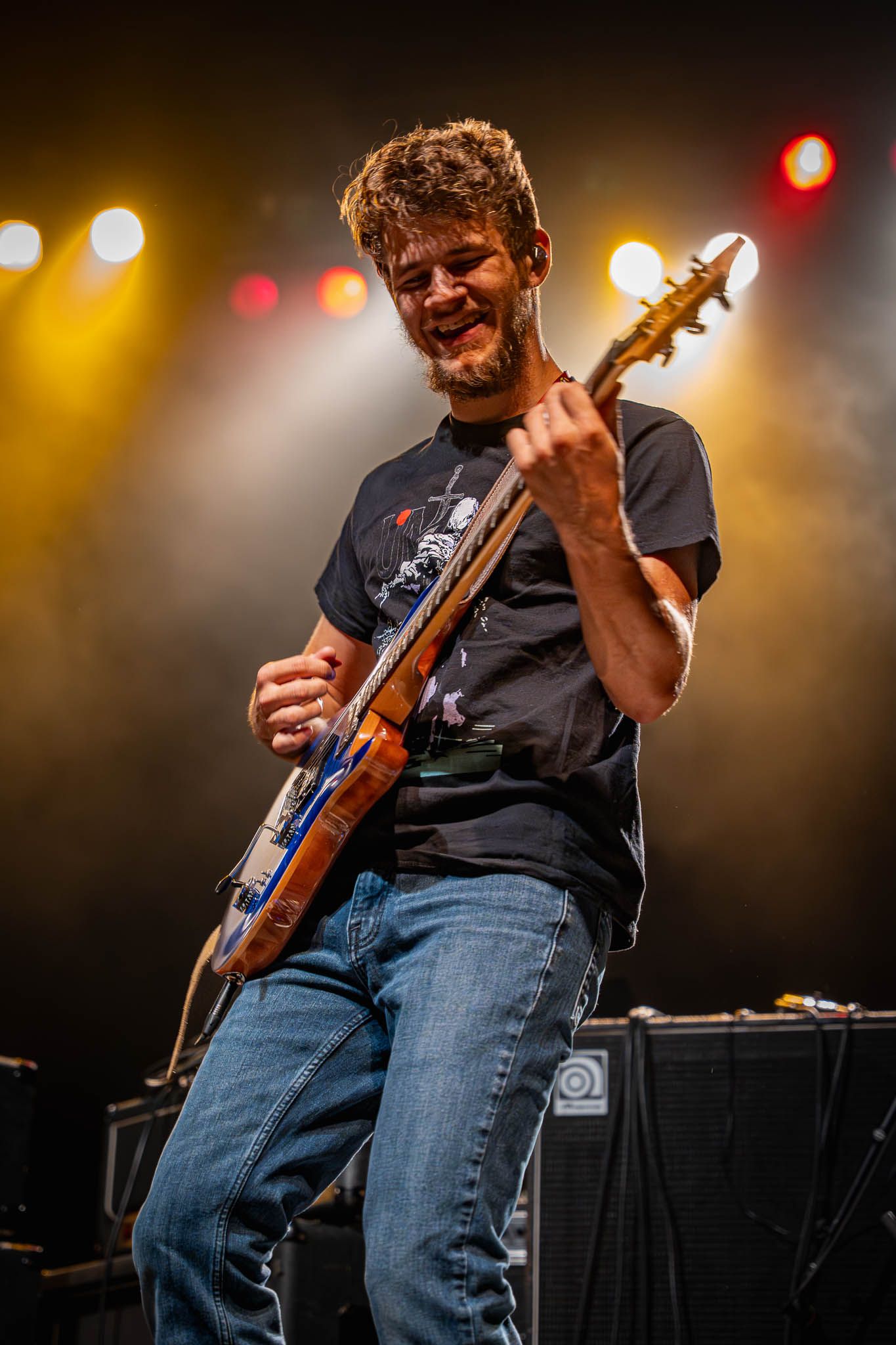 Guitarist in dark t-shirt and jeans performing under warm stage lights.