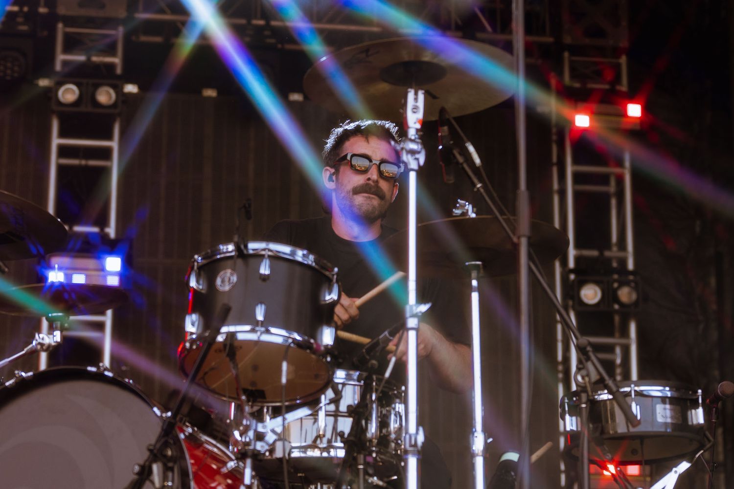 Concert stage setup with drum kit and lighting equipment visible in dramatic blue tones.
