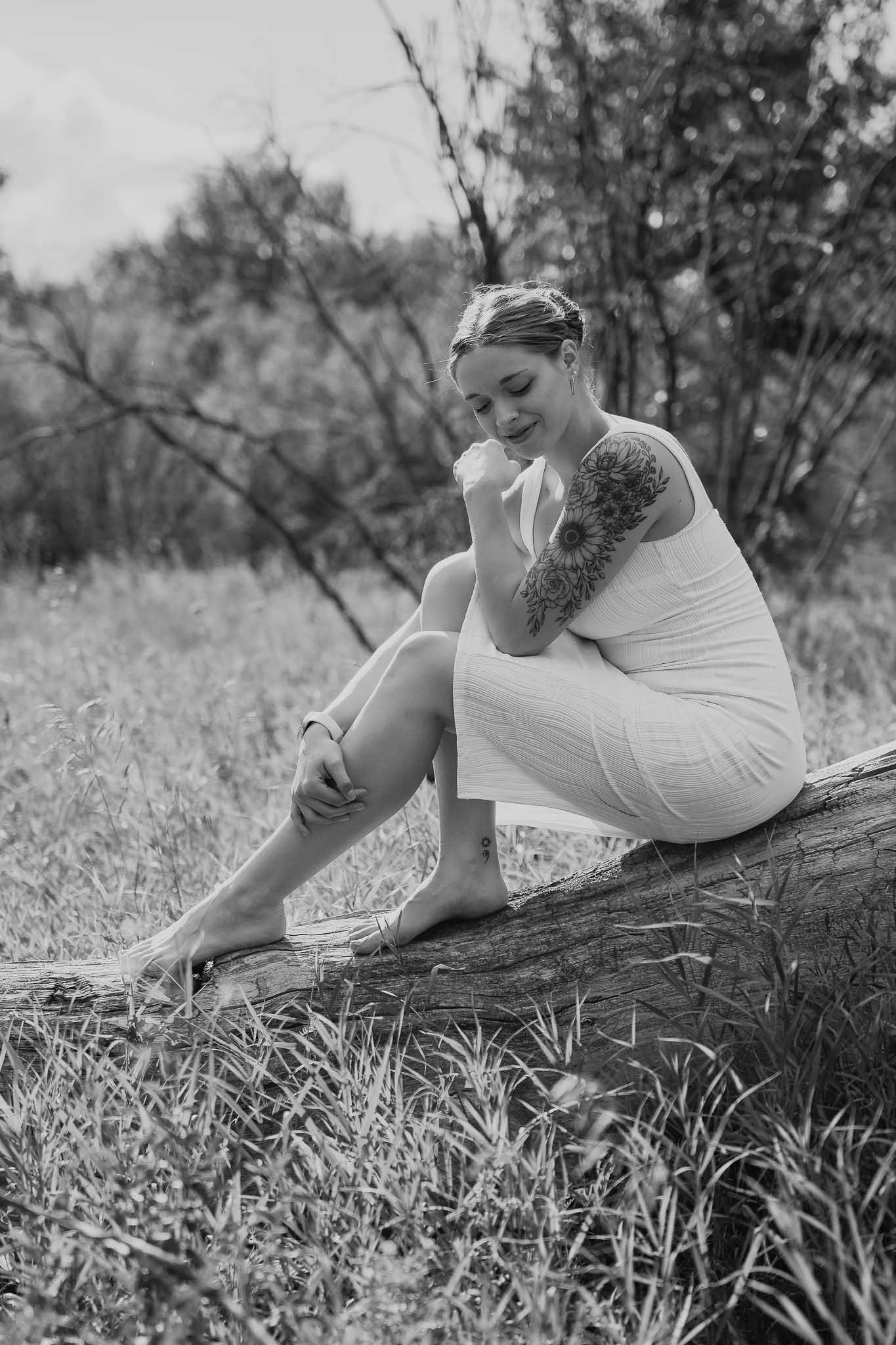 Woman in white dress poses elegantly on ground in black and white outdoor portrait.