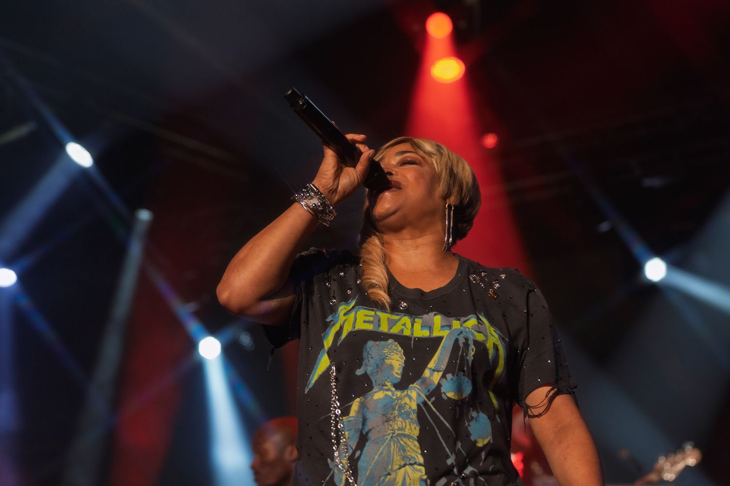 Concert performer singing into microphone under dramatic blue and red stage lighting.