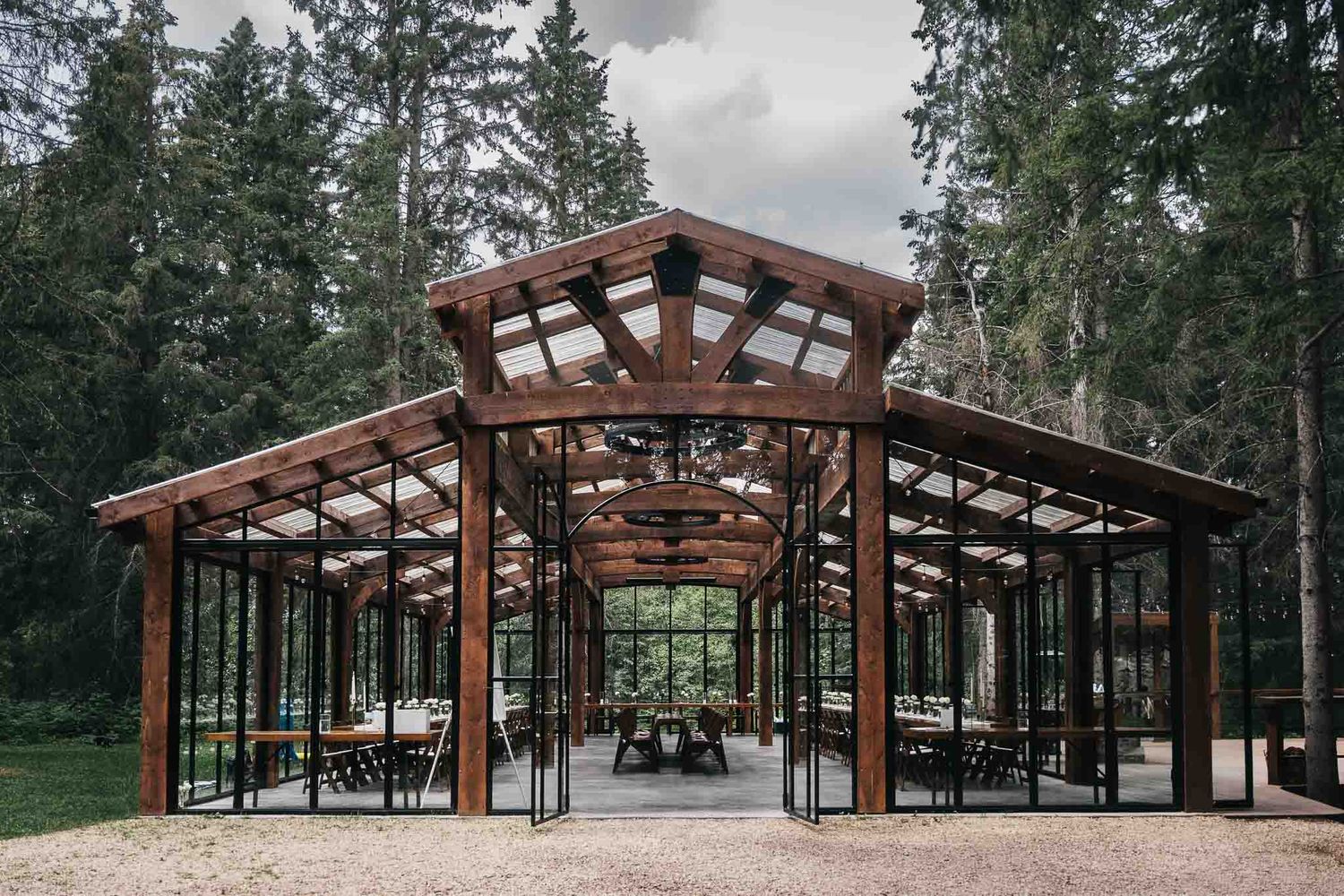 Outdoor wedding venue with wooden beams and glass walls surrounded by tall evergreen trees known as The Valley Weddings