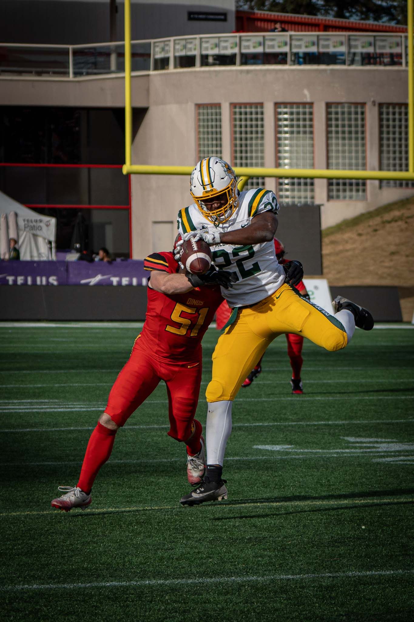 Football players in red and gold uniforms diving for tackle on artificial turf.