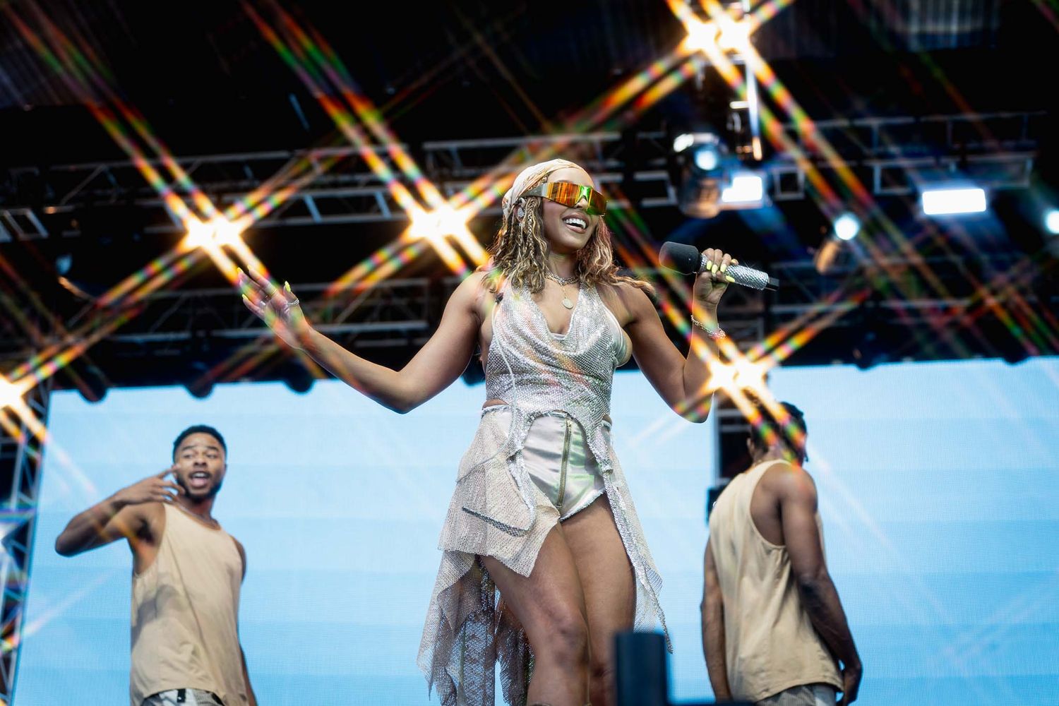 Concert performers in white outfits dance in formation under stage lights.